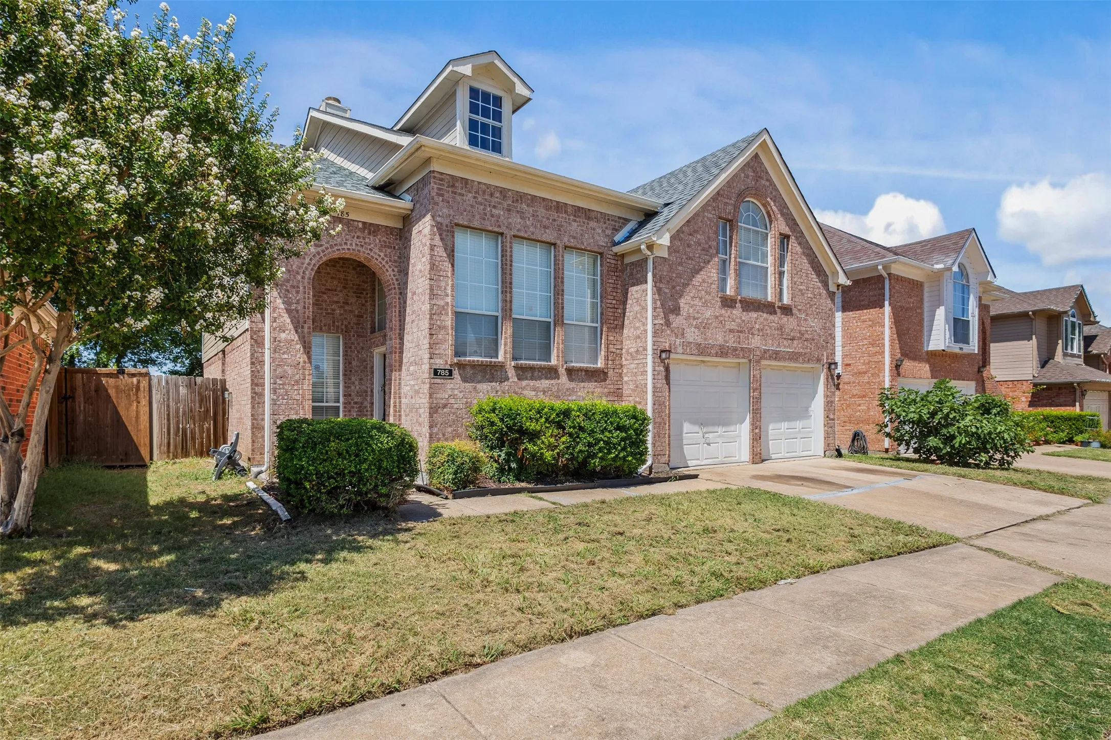 Brick facade residence featuring an arched entry, a two-car garage with white doors, and a dormer window