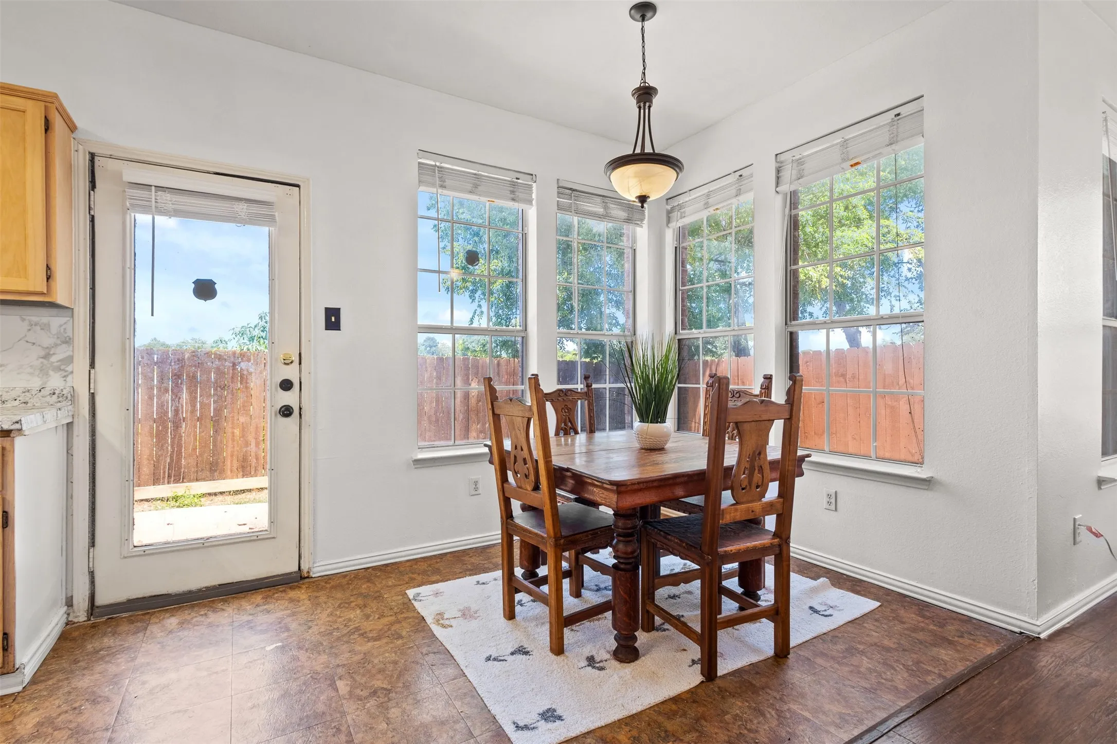 Bright dining area with multiple windows offering exterior views, wood-finish flooring, a built-in light fixture, and a glass-paneled exterior door