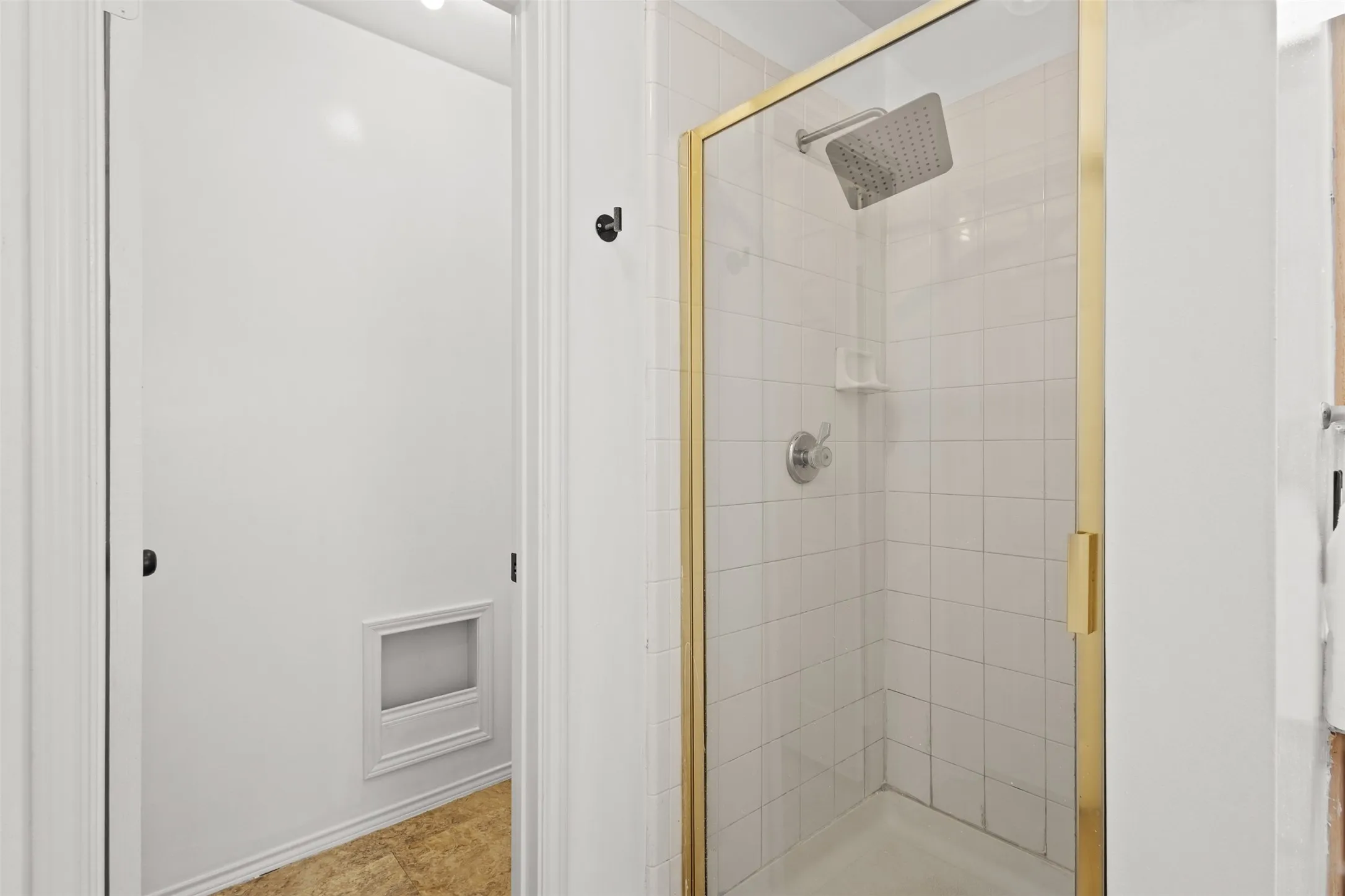 Glass-enclosed shower with gold-tone framing, rain shower head, and white square tile surround