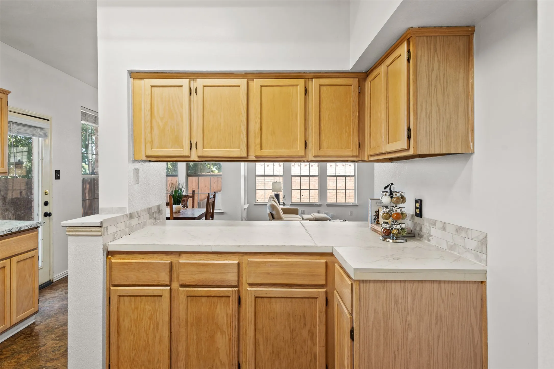Kitchen pass-through featuring light wood cabinetry, light-colored countertops, and a subway tile backsplash