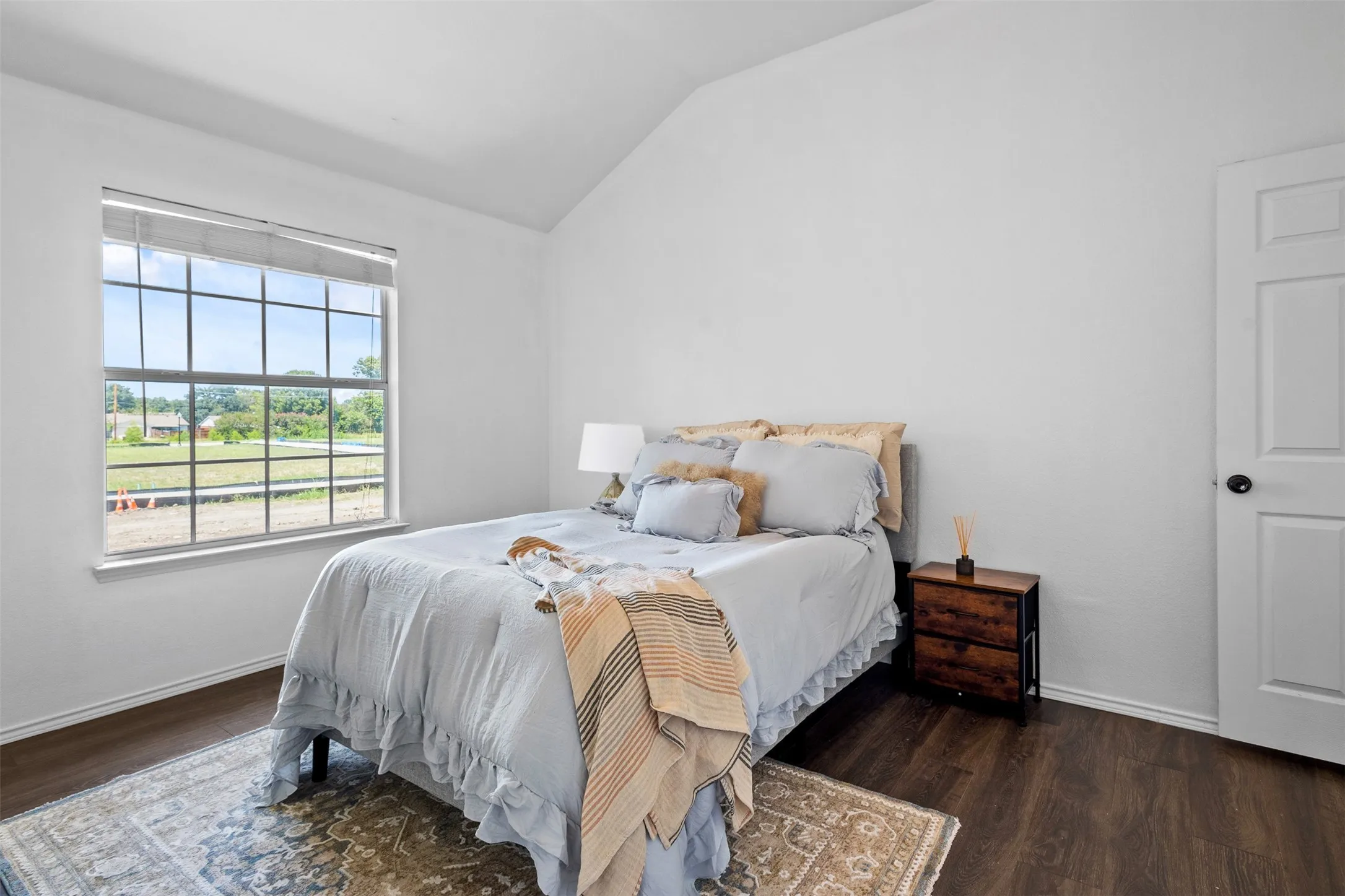 Spacious room featuring vaulted ceilings, a large grid-pattern window, wood-finish flooring, and white walls