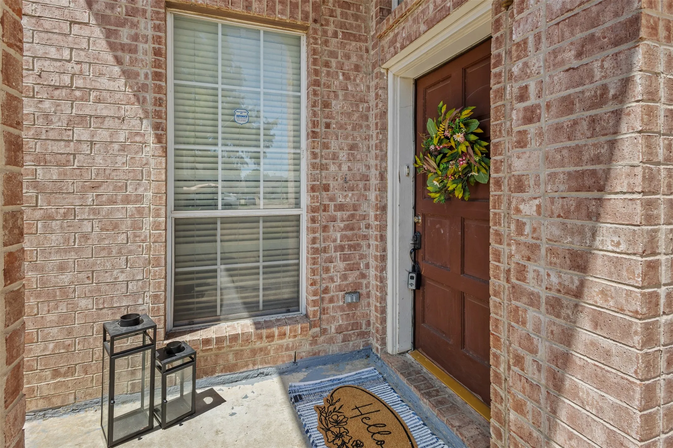 Brick exterior with a paneled front door, an adjacent window with blinds, and a concrete entry pad