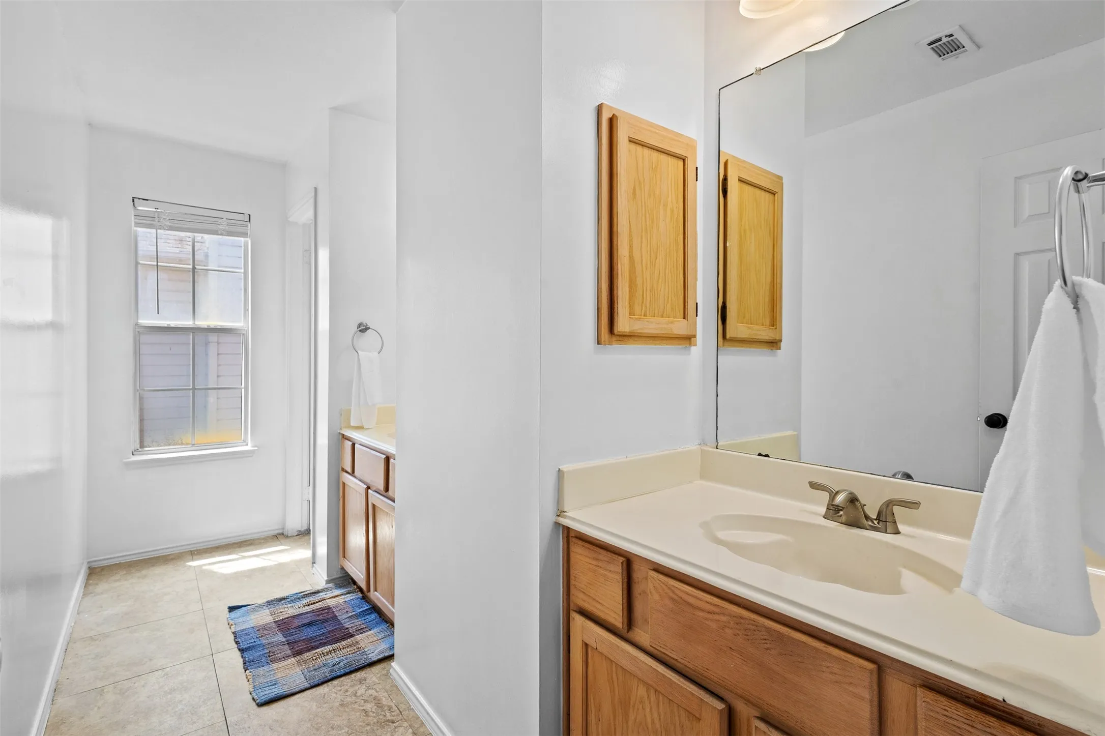 Bathroom featuring a single vanity with wood-finish cabinetry, a built-in sink, and a large mirror