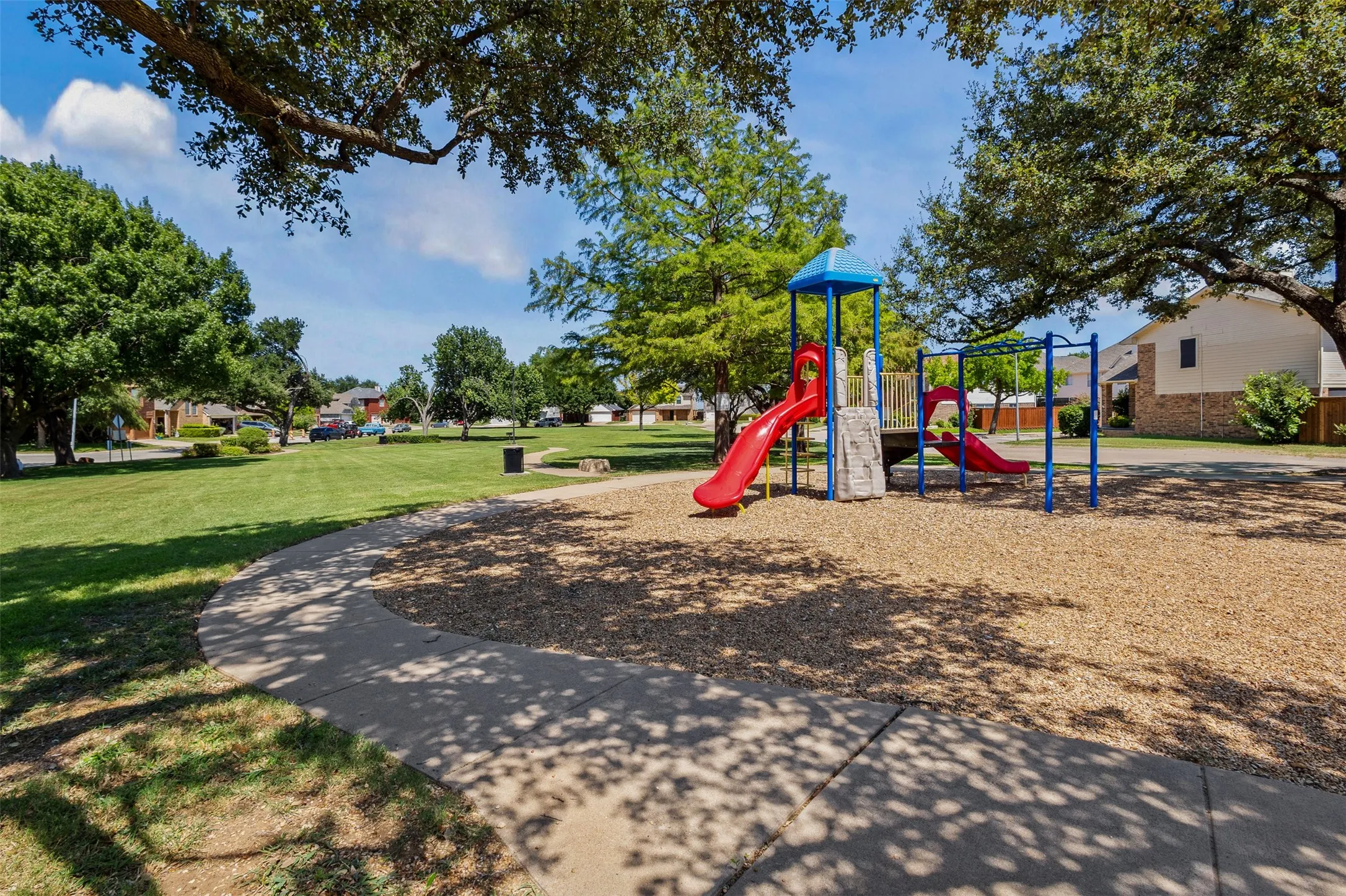 Outdoor playground featuring a red slide, blue-framed monkey bars, and a climbing wall, set on a wood chip surface