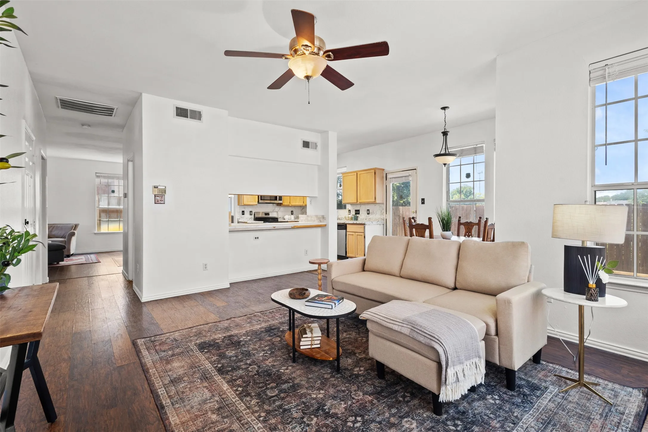 Open-concept living space featuring wood-finish flooring, a ceiling fan with integrated lighting, and multiple windows
