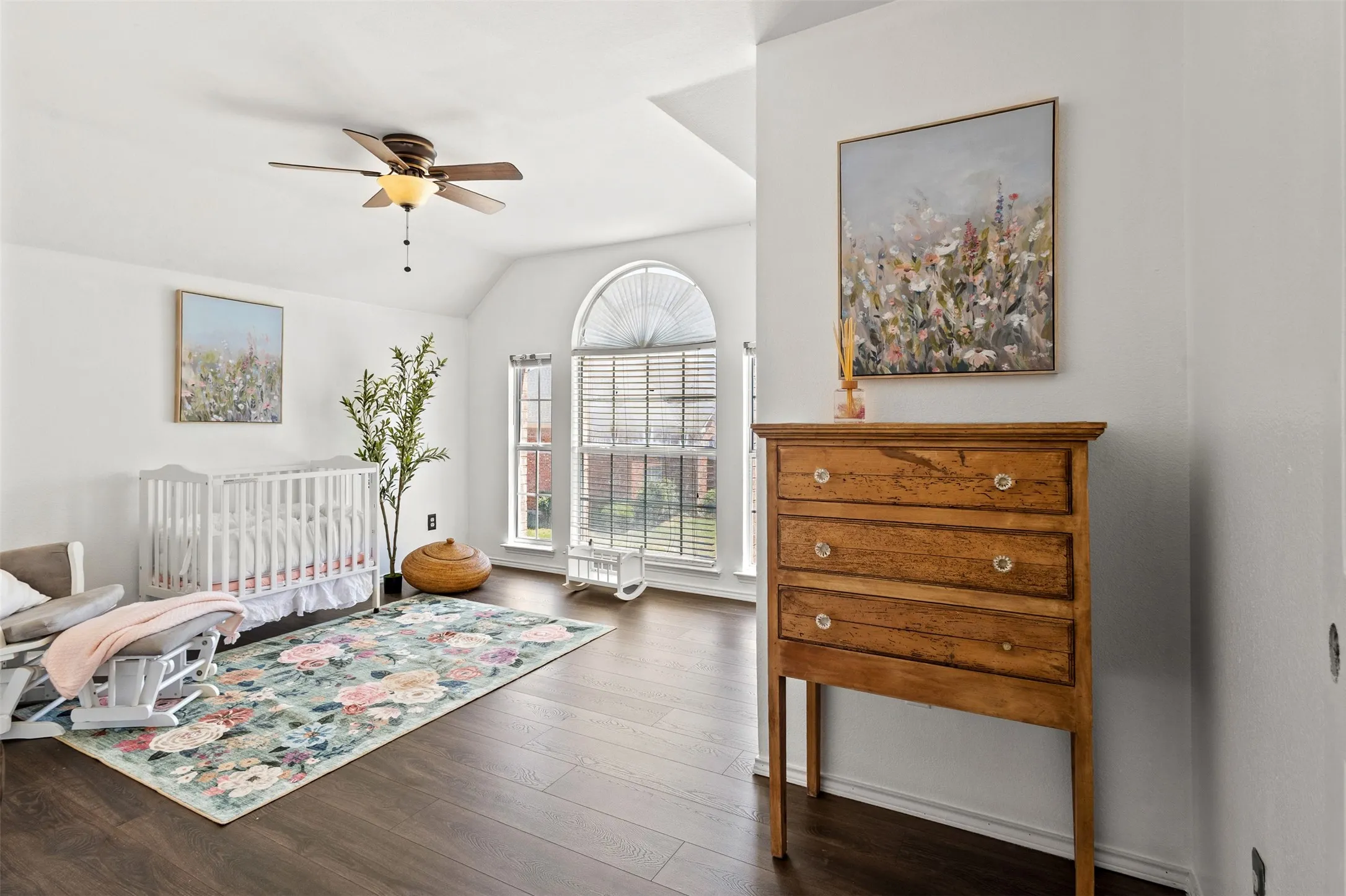 Spacious room featuring vaulted ceilings, wood-finish flooring, and arched windows with horizontal blinds