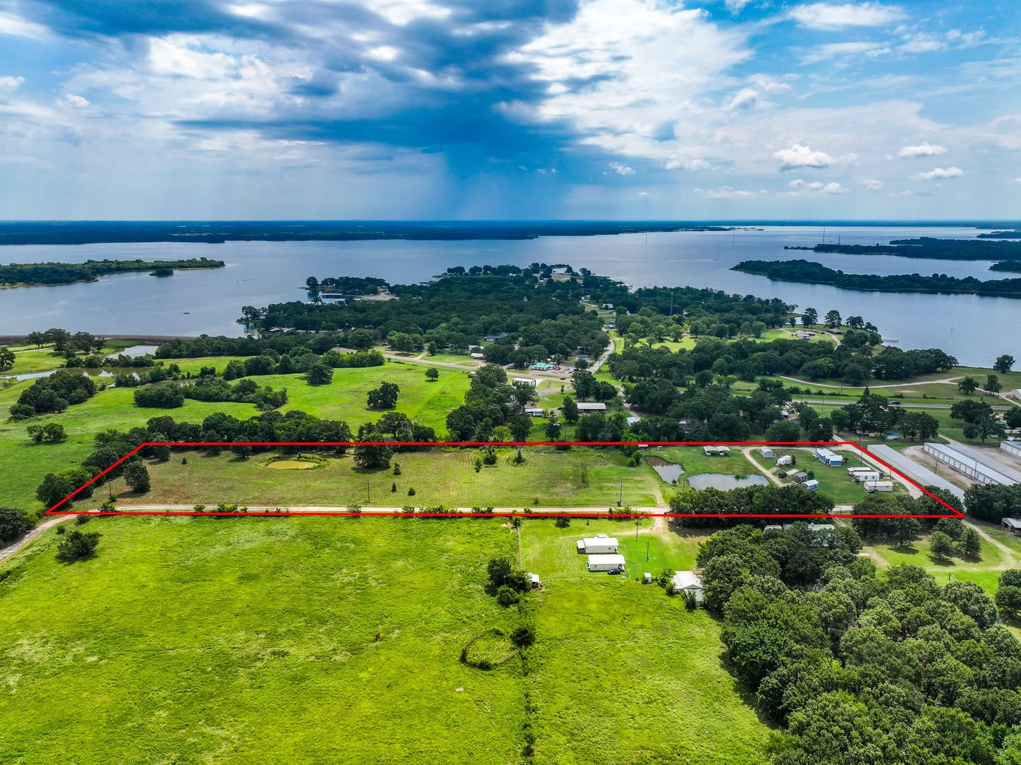Expansive acreage parcel featuring a perimeter boundary, mature trees, open green spaces, and a prominent lake backdrop