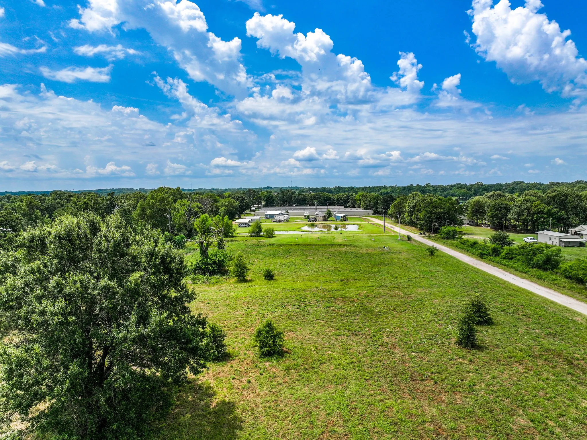 Expansive undeveloped land featuring a gravel road, scattered mature trees, and a visible pond