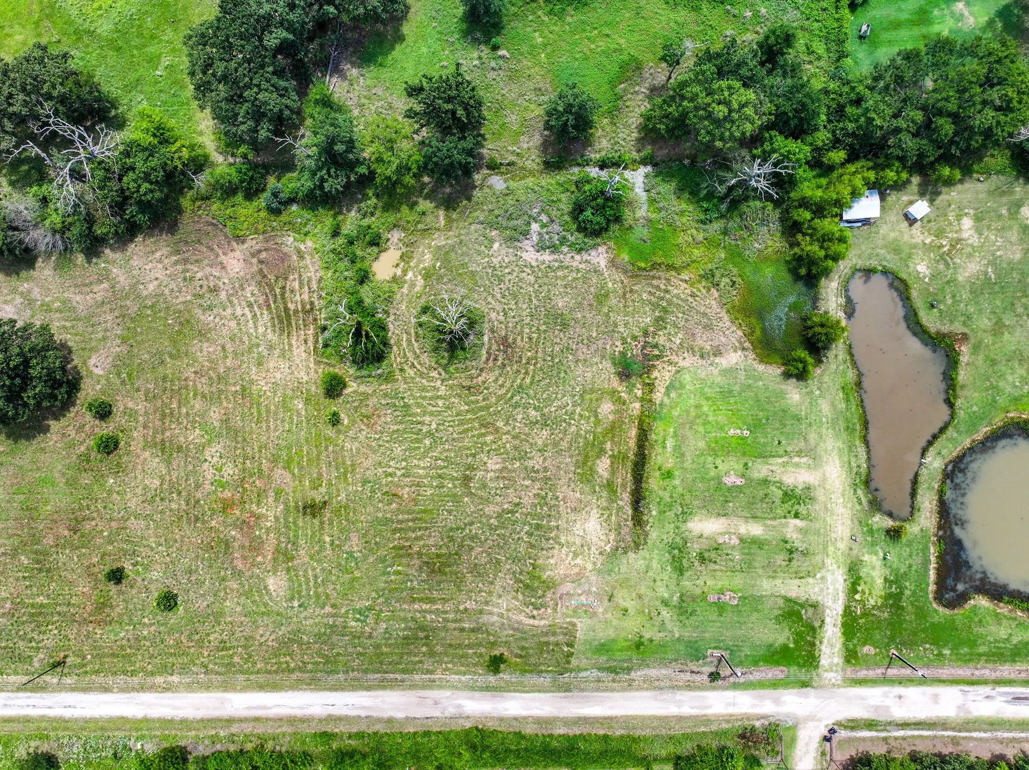 Expansive land parcel featuring natural ponds, scattered mature trees, and a dirt road bordering the property