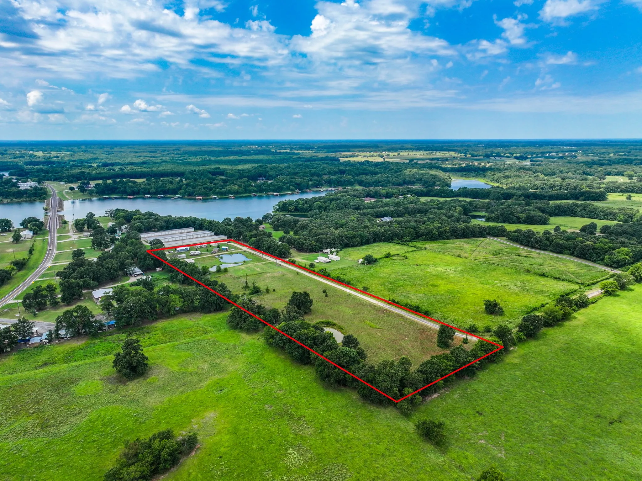 Expansive land parcel featuring a visible red boundary line, two distinct ponds, surrounding mature trees, and direct proximity to a body of water with a bridge