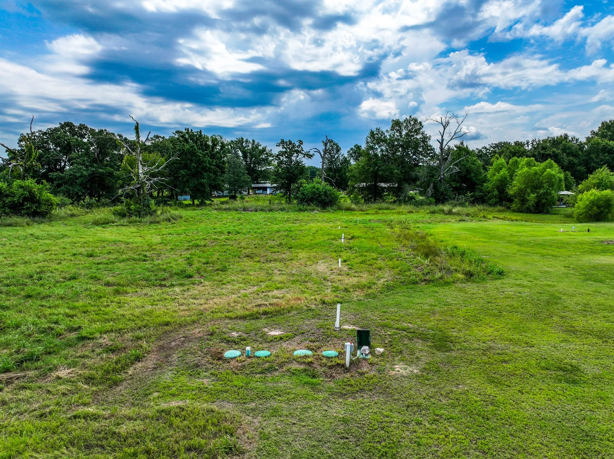 Expansive grassy terrain featuring established trees along the perimeter and visible septic system components