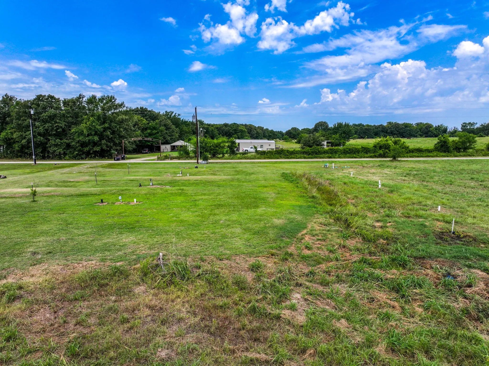 Expansive green space with distant tree lines, utility poles, and a partial view of a residential structure