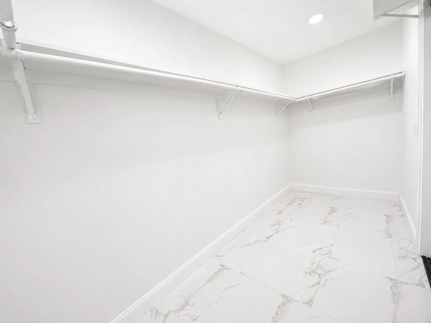 Walk-in closet featuring white marble-look tile flooring, white walls, and built-in white shelving and hanging rods
