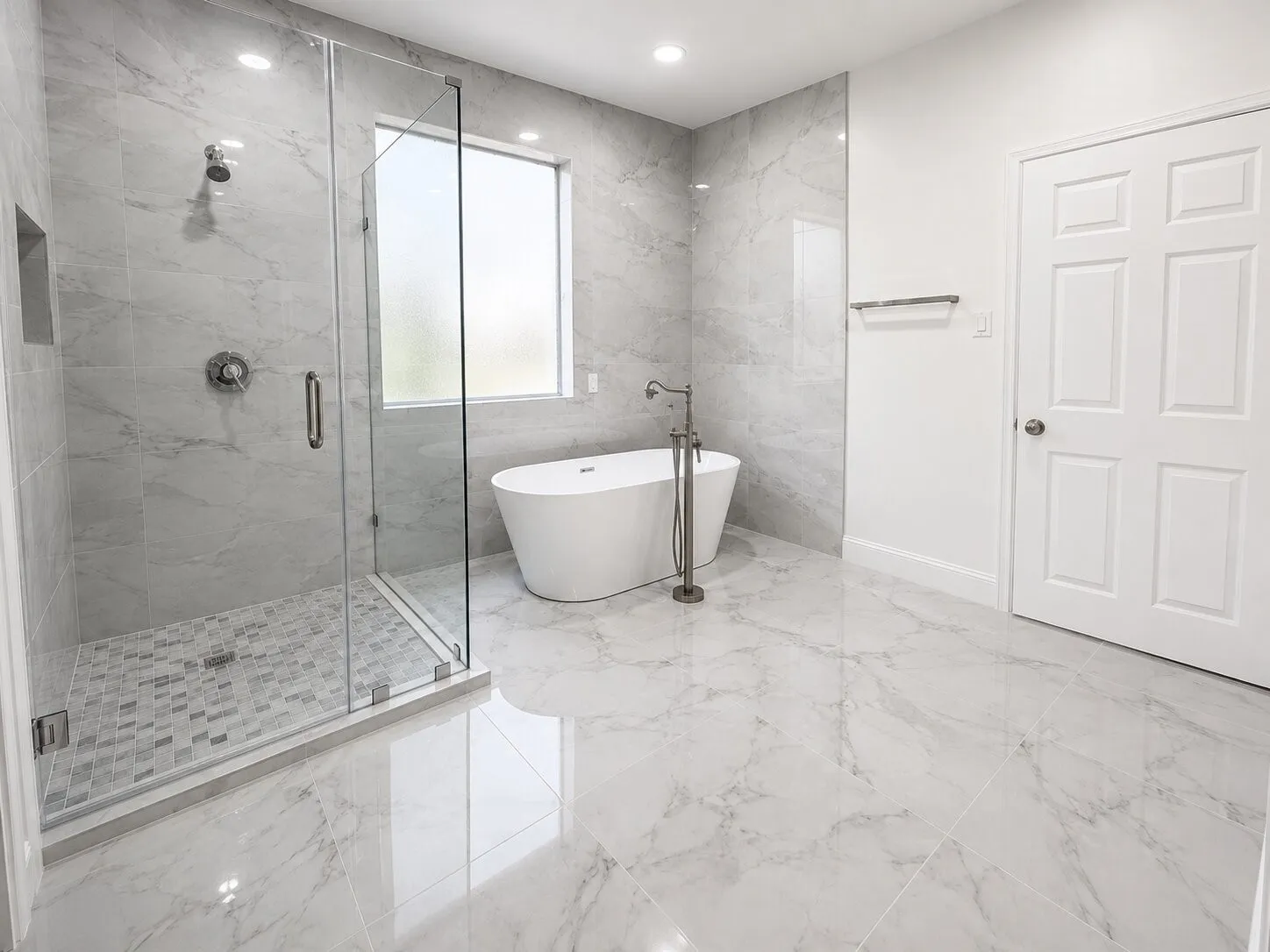 Spacious bathroom featuring a frameless glass walk-in shower with mosaic tile pan, a freestanding soaking tub with floor-mounted filler, and large format marble-look tile flooring