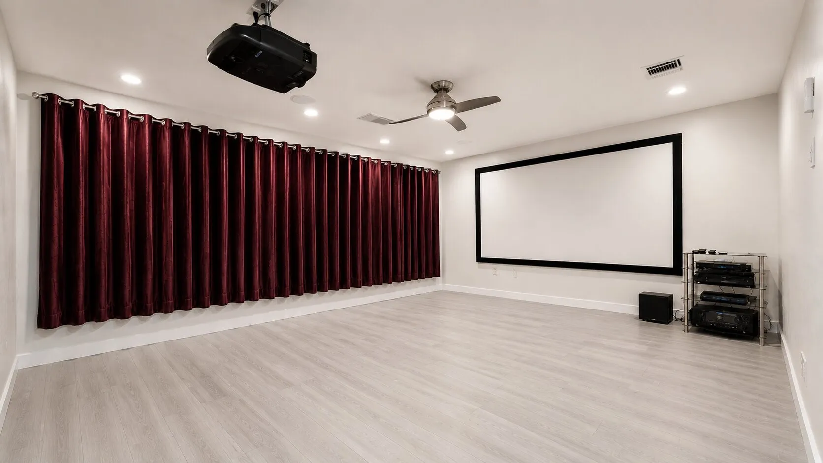 Dedicated media room featuring a large projection screen, mounted projector, and extensive burgundy velvet privacy curtains
