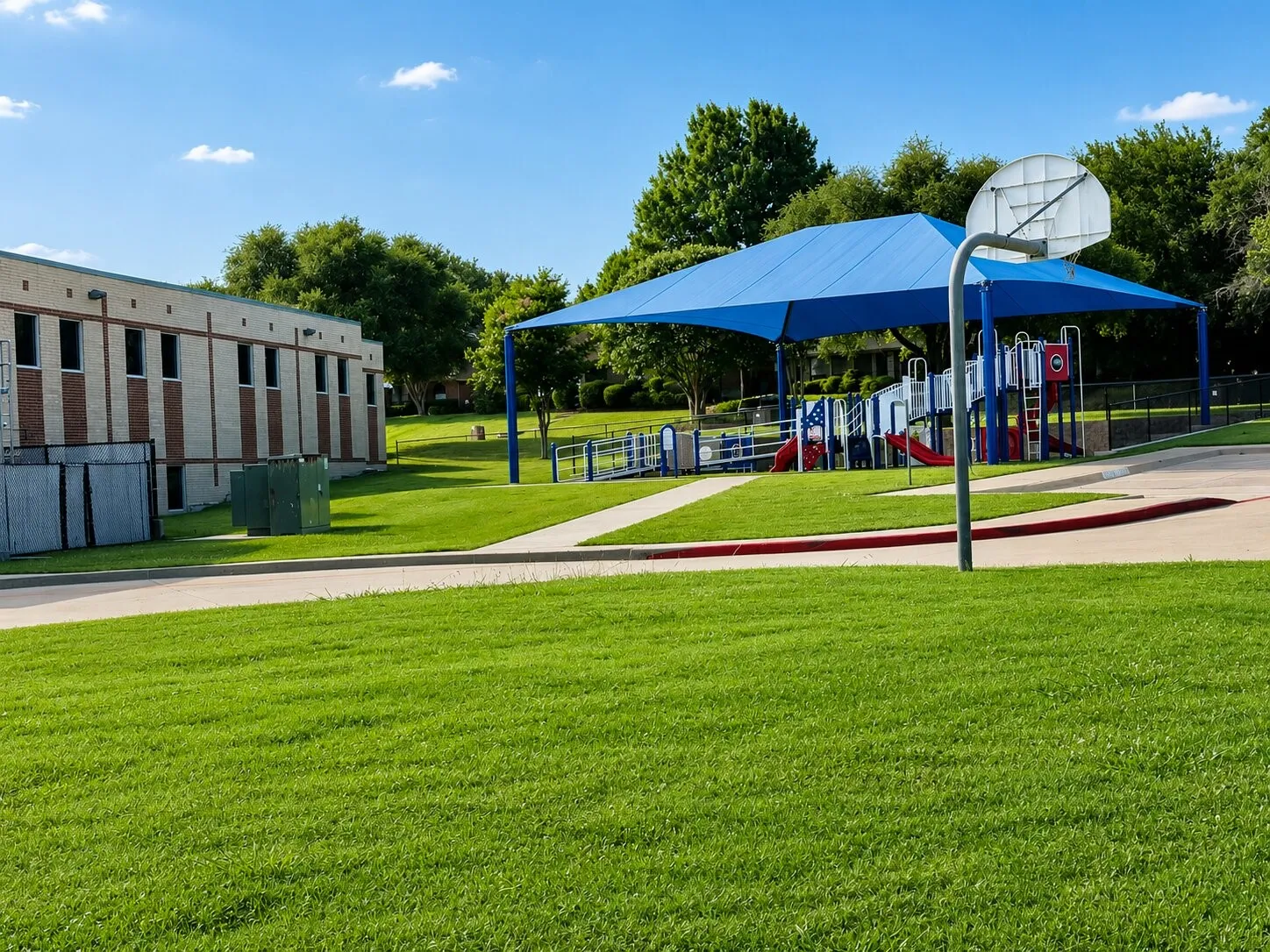 Playground area featuring a blue canopy, multiple slides, climbing structures, and a basketball hoop