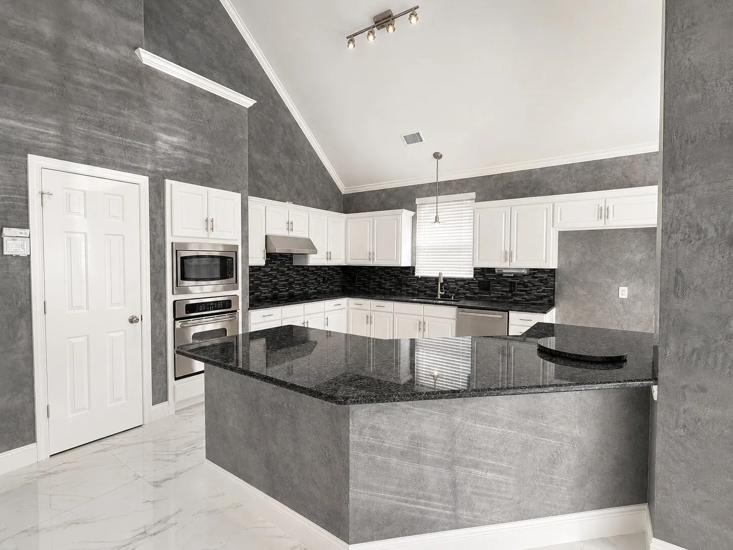 Kitchen featuring a vaulted ceiling with track lighting, white cabinetry, dark stone countertops, stainless steel appliances, and a central island with a breakfast bar