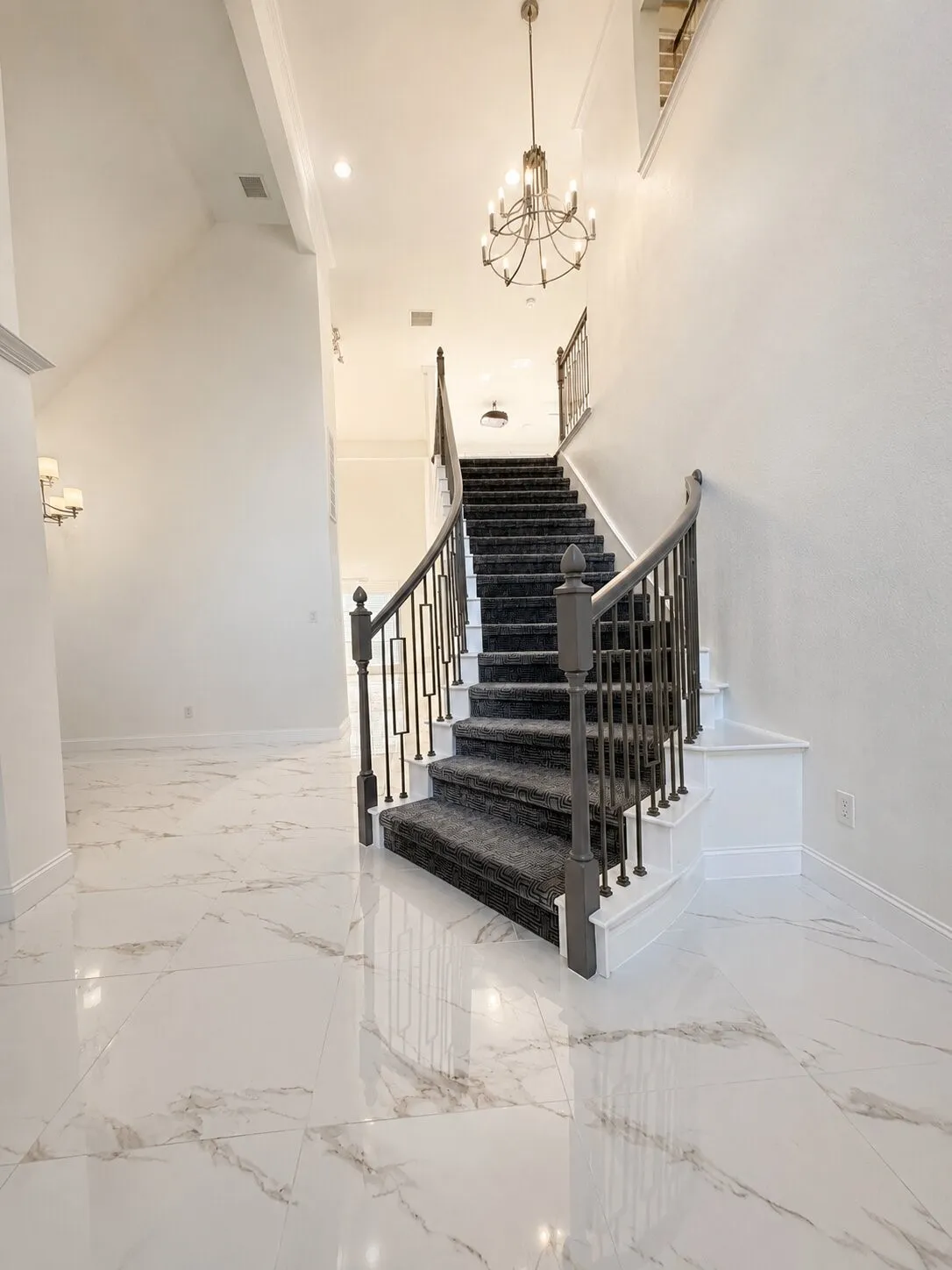 Grand entryway featuring a curved staircase with dark balusters, textured tread covering, and a high ceiling with a classic chandelier