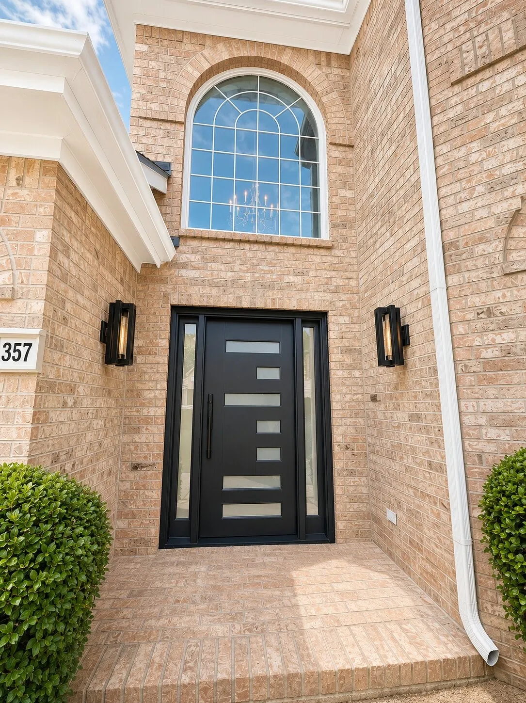Brick exterior featuring a black entry door with frosted glass inserts, flanked by matching black sconces