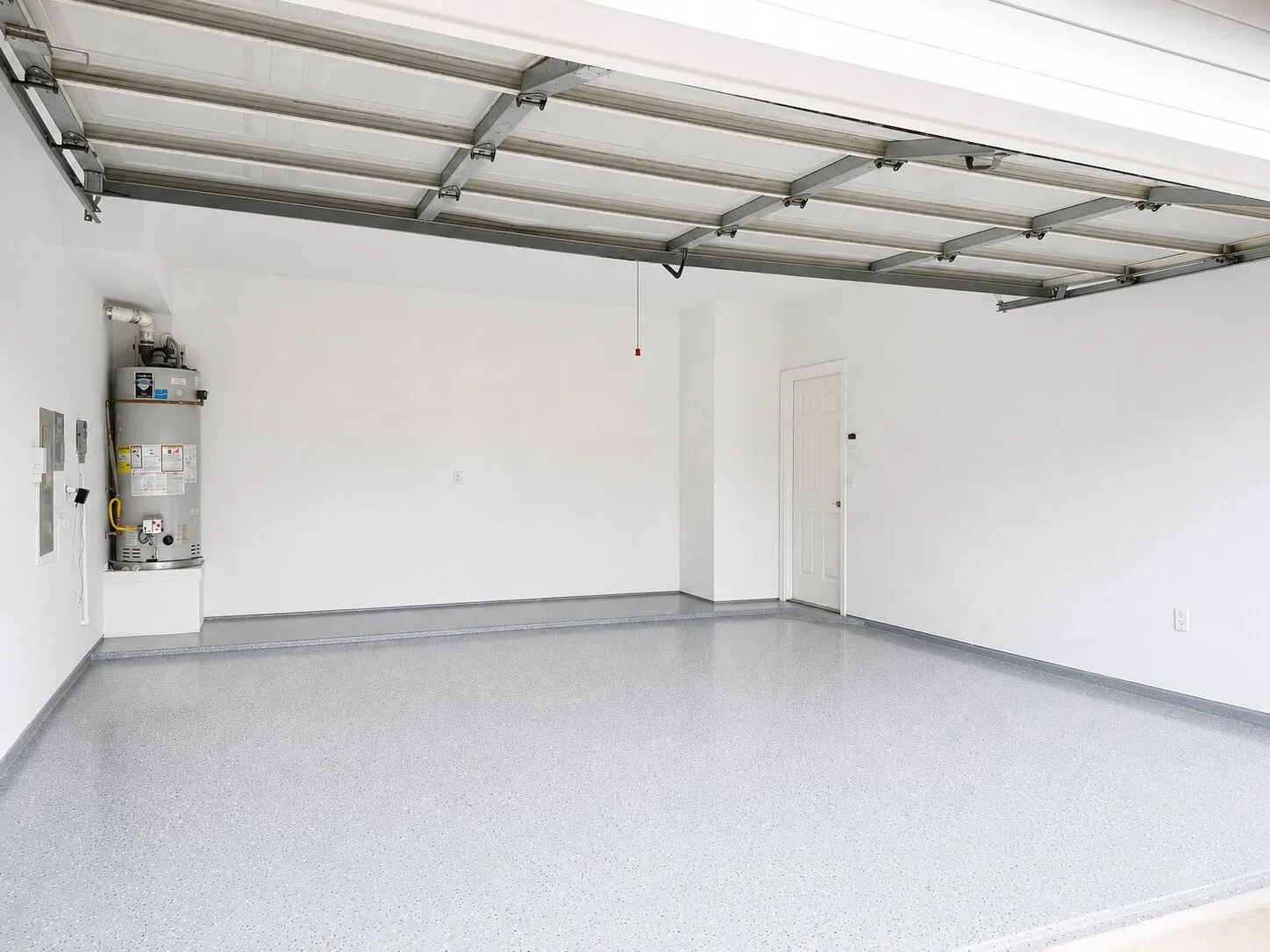 Spacious garage with light gray speckled epoxy flooring, white painted walls, and a white interior door