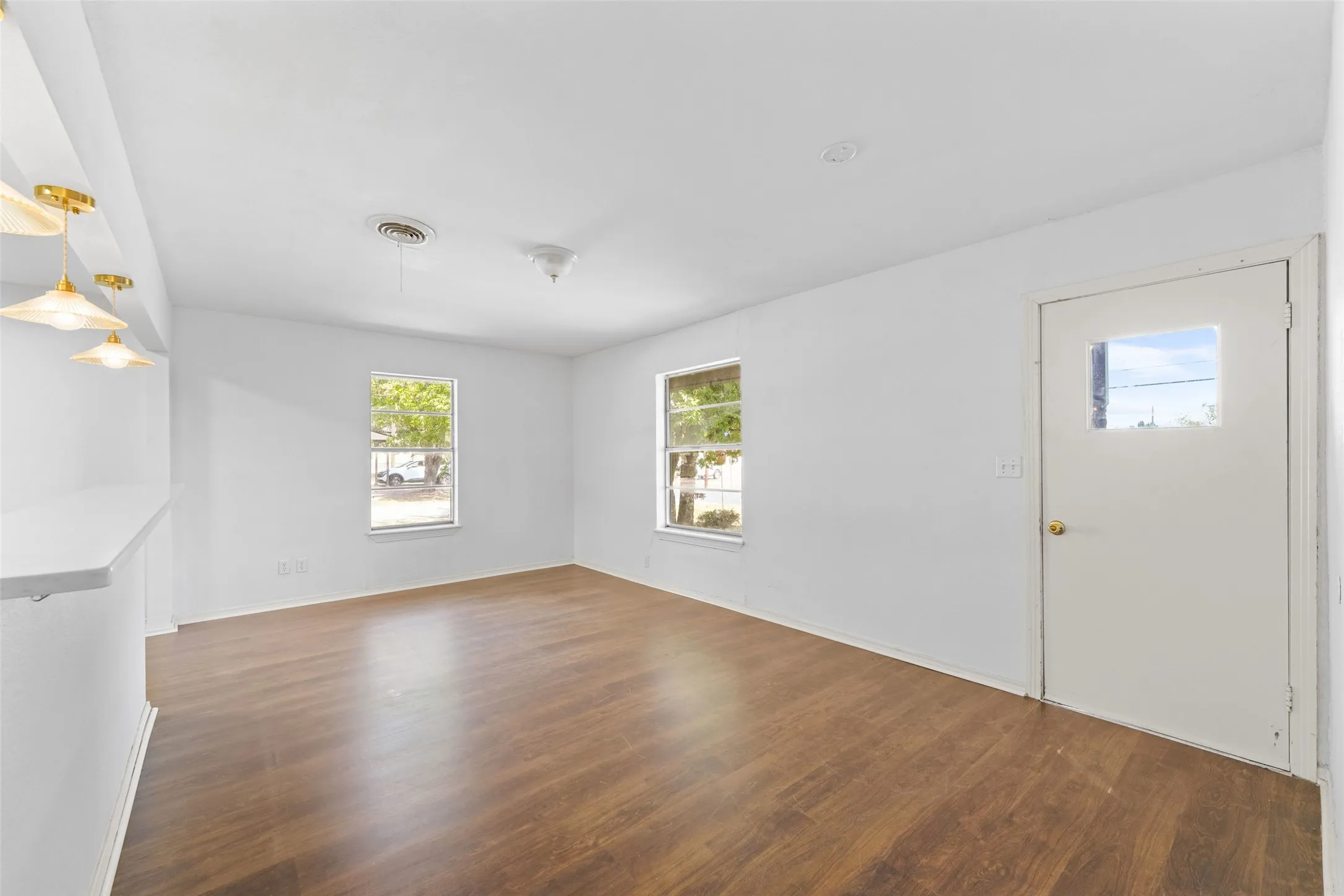Wood-finish flooring, white walls, multiple windows, built-in counter, and ceiling-mounted light fixtures