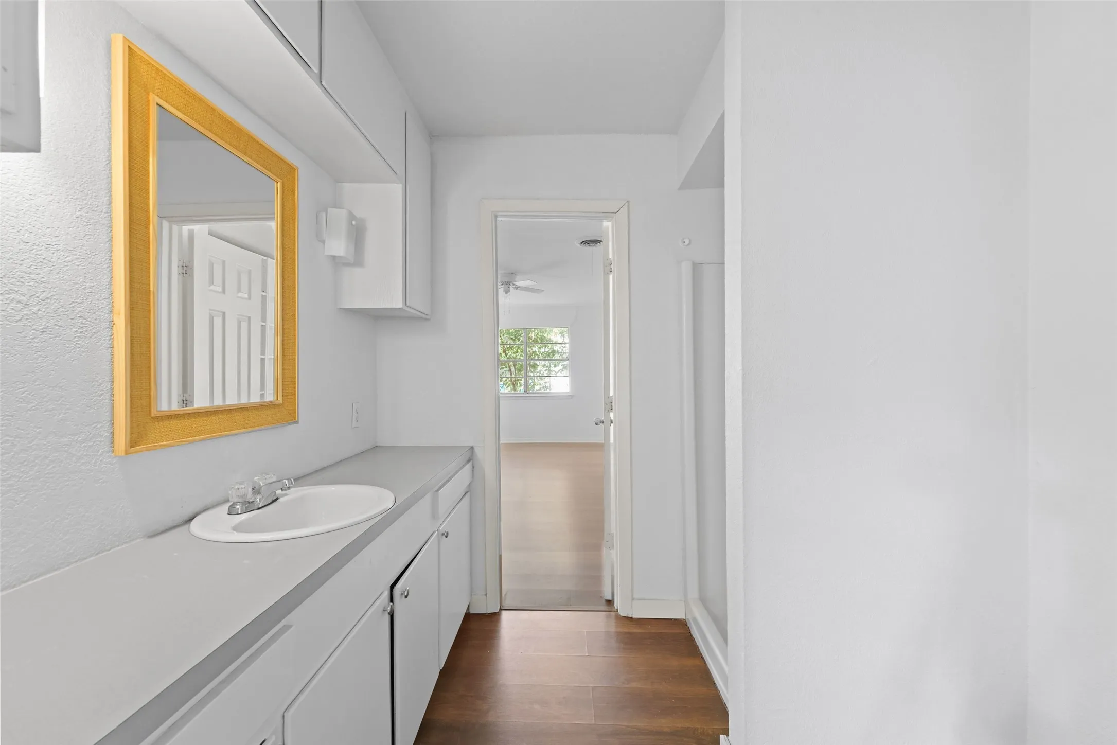 Integrated vanity with a single basin sink, wall-mounted mirror, white cabinetry, and overhead storage