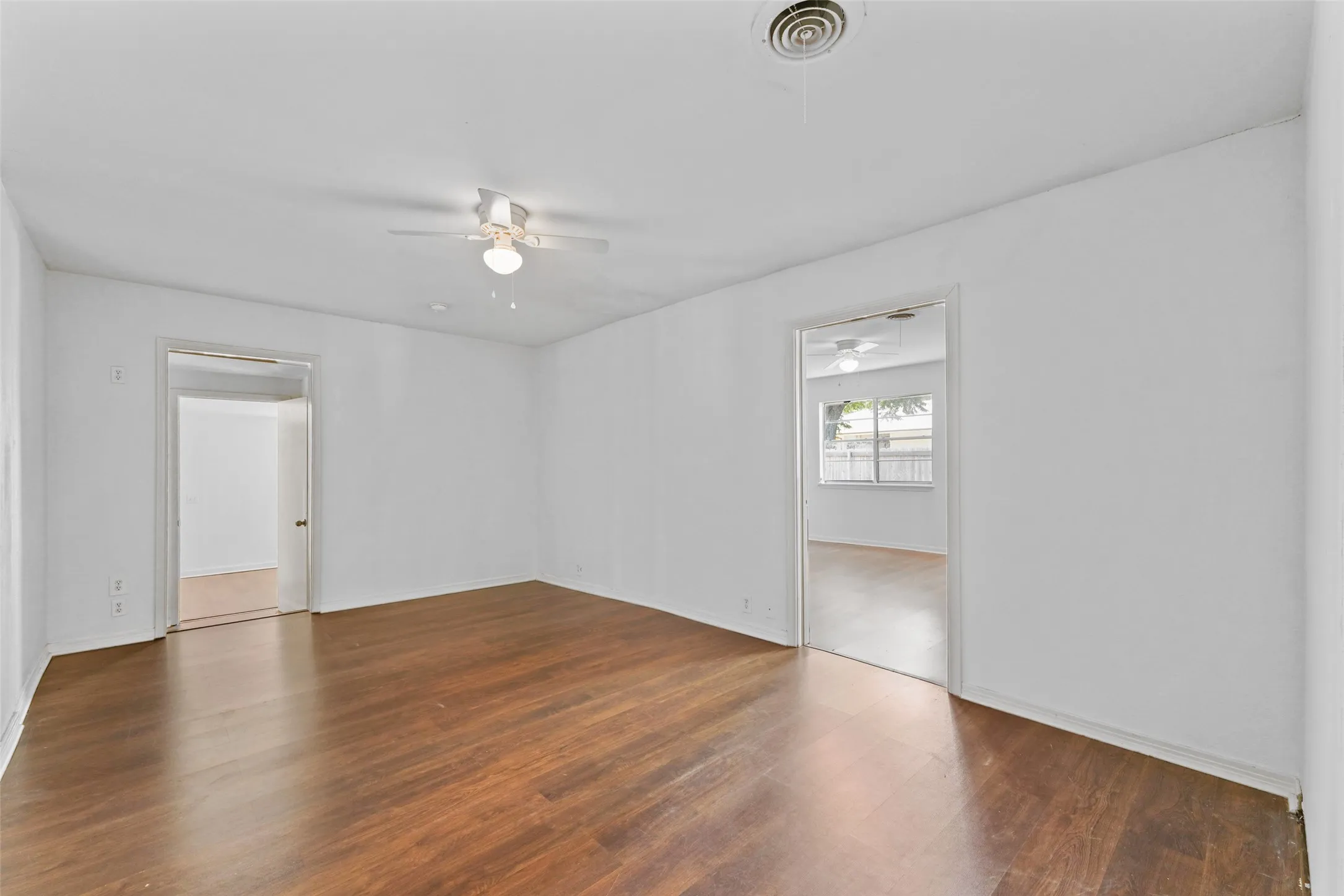 Wood-finish flooring throughout, white walls, and a ceiling fan with integrated lighting