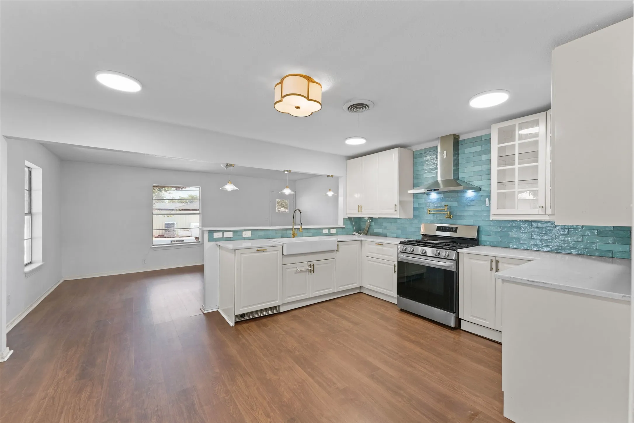 Kitchen with wood-finish flooring, white cabinetry, integrated stainless steel range with hood, and a teal tile backsplash
