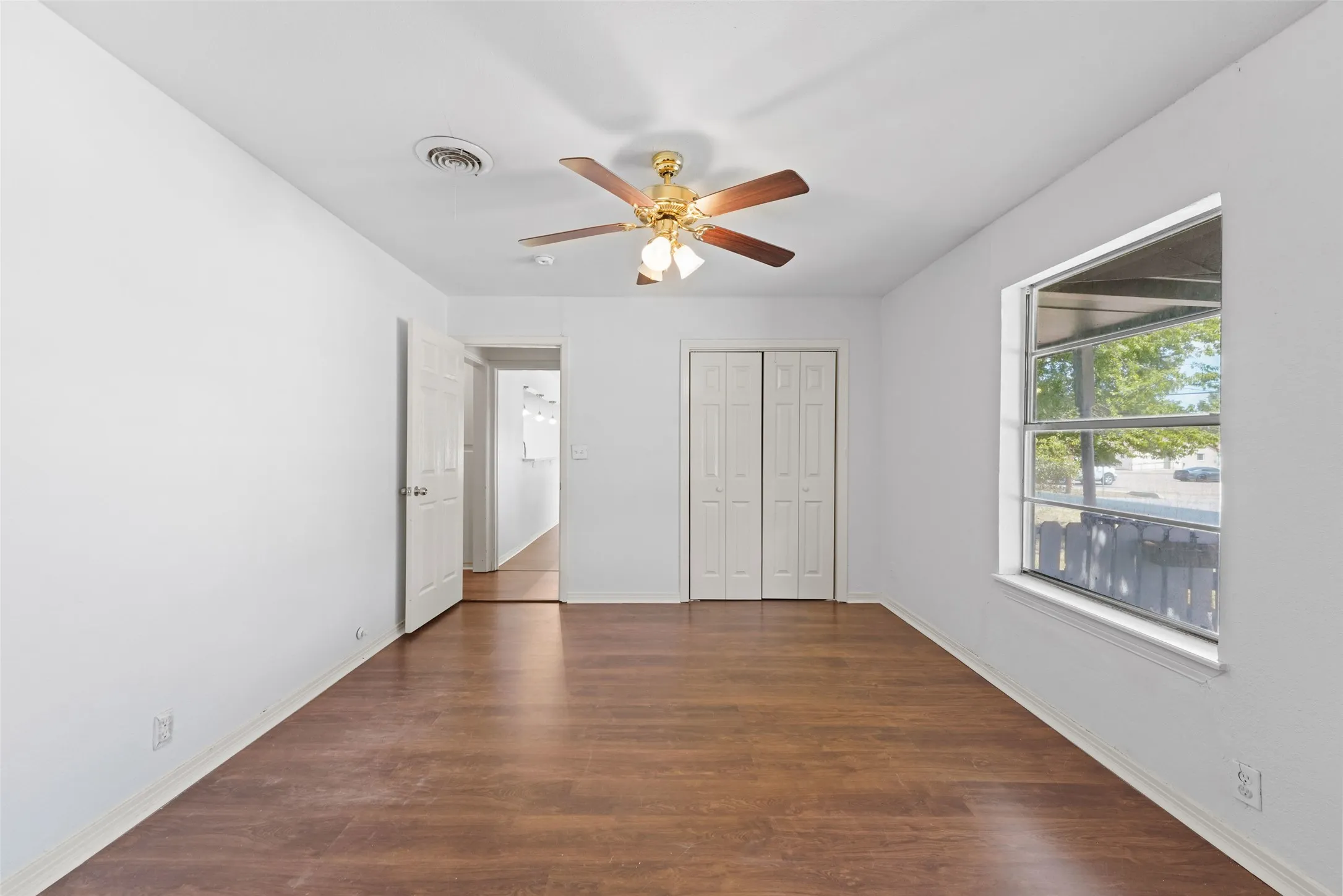 Wood-finish flooring, ceiling fan with integrated lighting, white interior walls, white bi-fold closet doors, and a window with exterior visibility