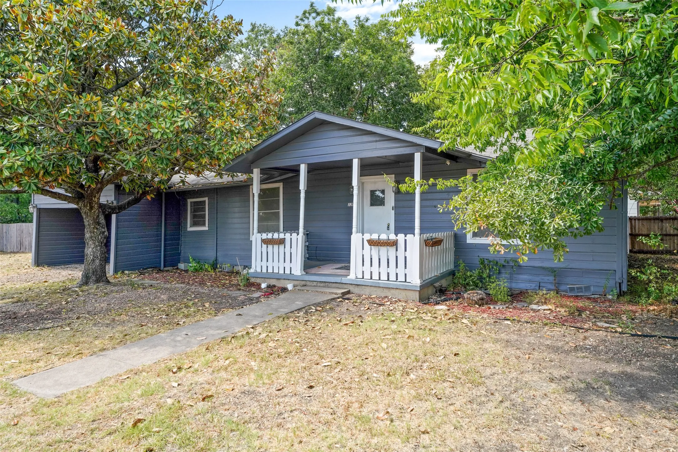 Exterior featuring a covered front porch, white railing with planters, gray siding, and a concrete walkway