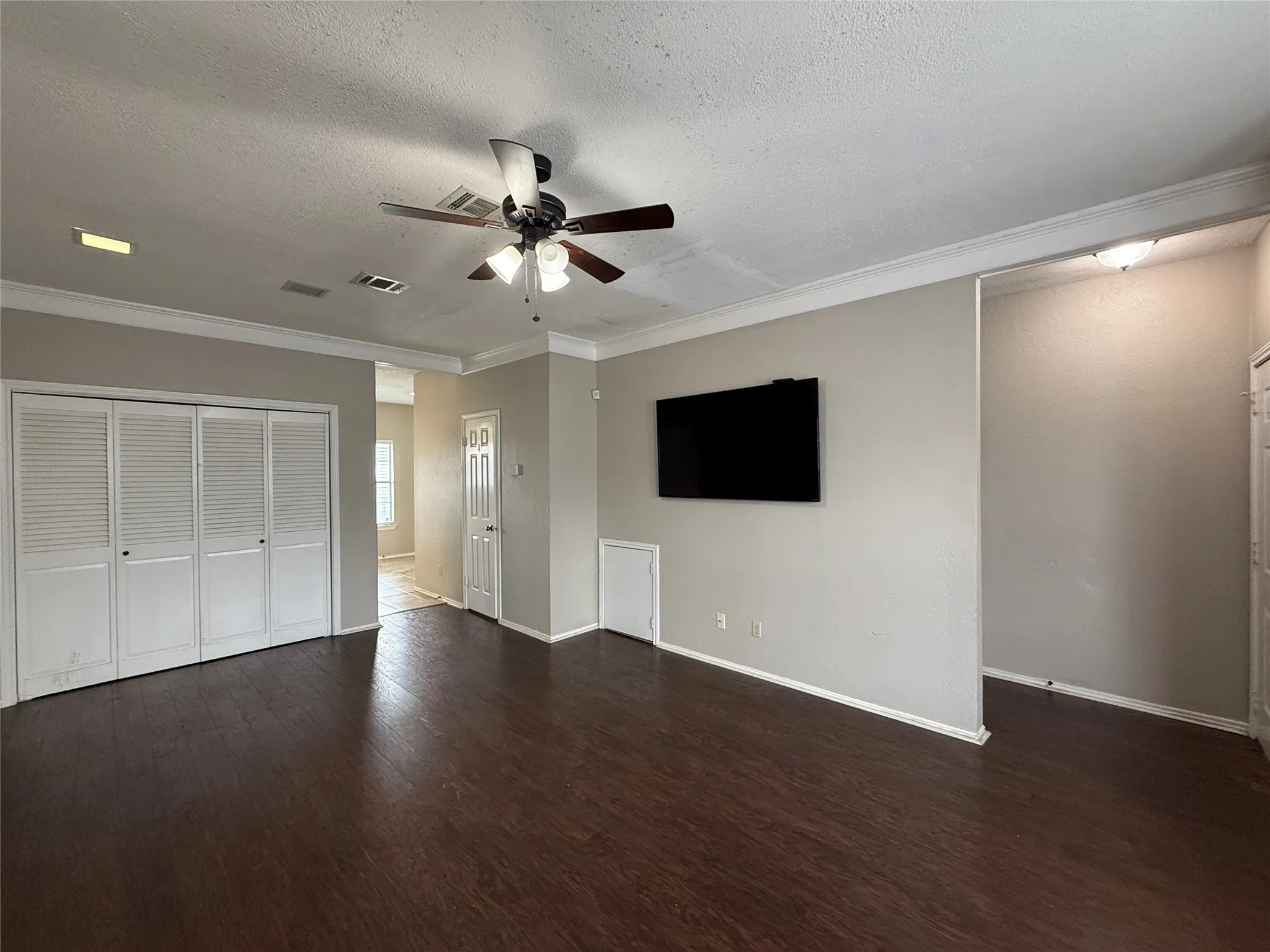 Unfurnished living room featuring a ceiling fan, wood finished floors, crown molding, and a textured ceiling
