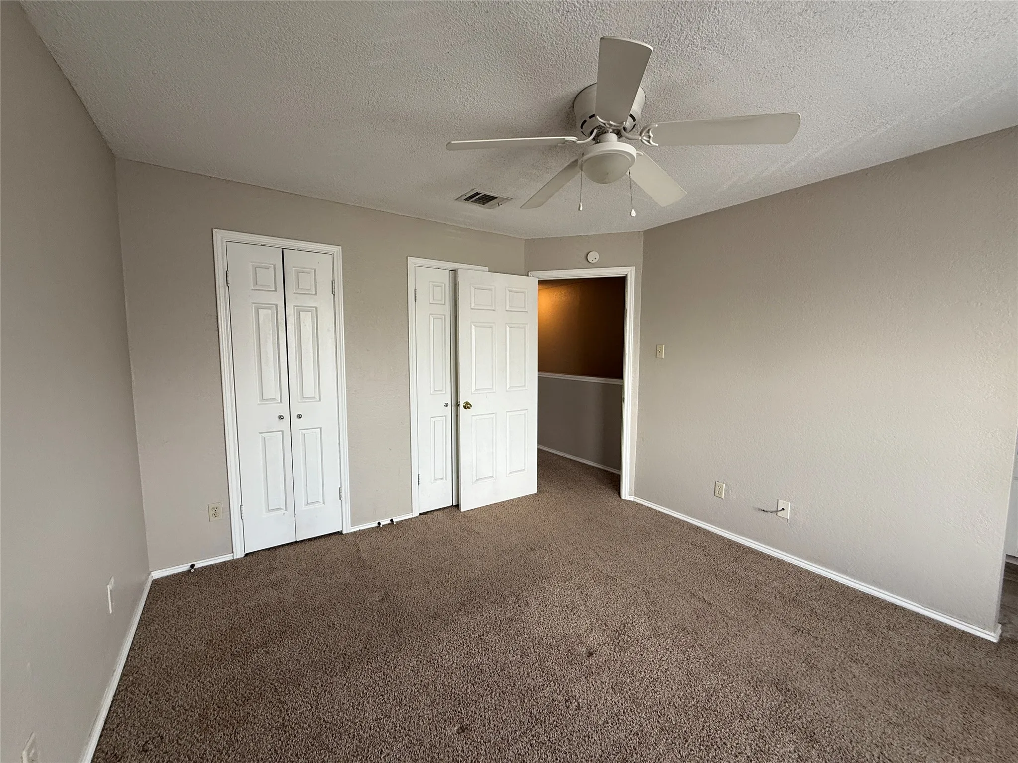 Unfurnished bedroom with carpet flooring, two closets, a textured ceiling, and ceiling fan