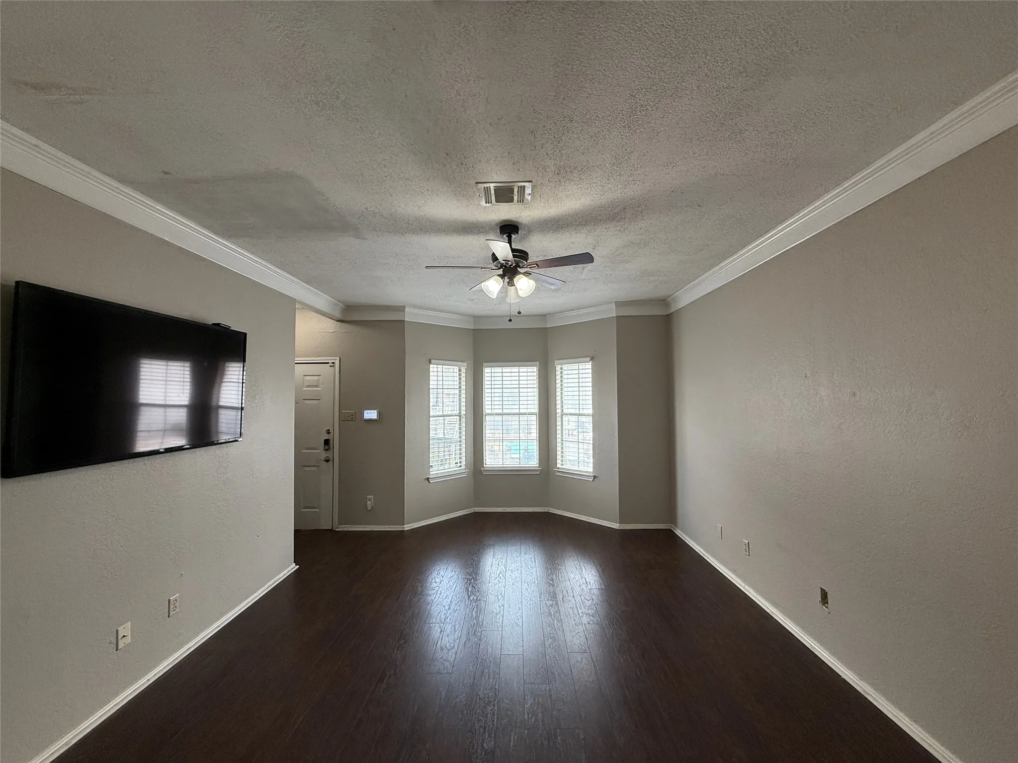 Unfurnished room featuring a ceiling fan, a textured ceiling, ornamental molding, and wood finished floors