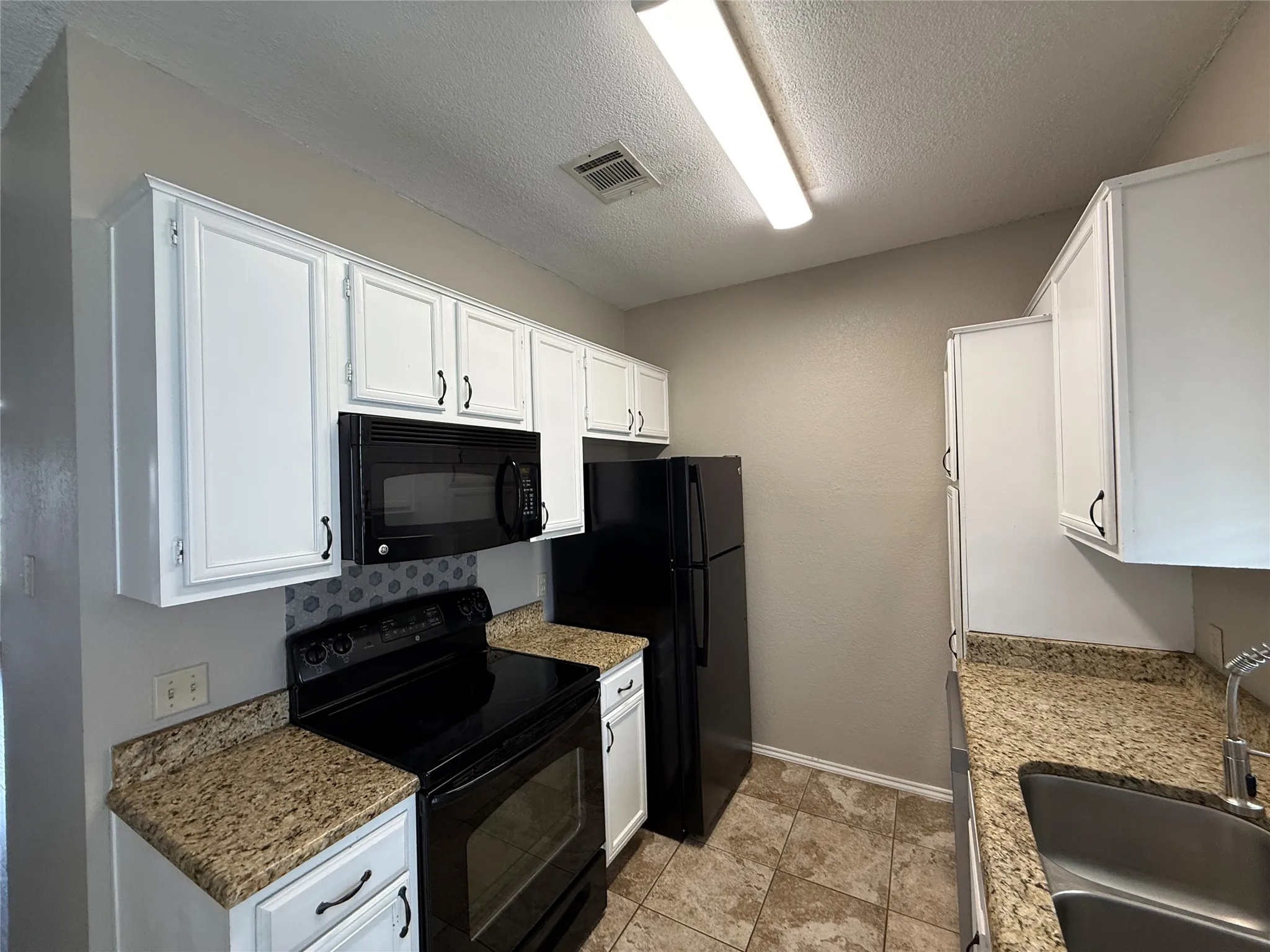 Kitchen with black appliances, white cabinets, and a textured ceiling