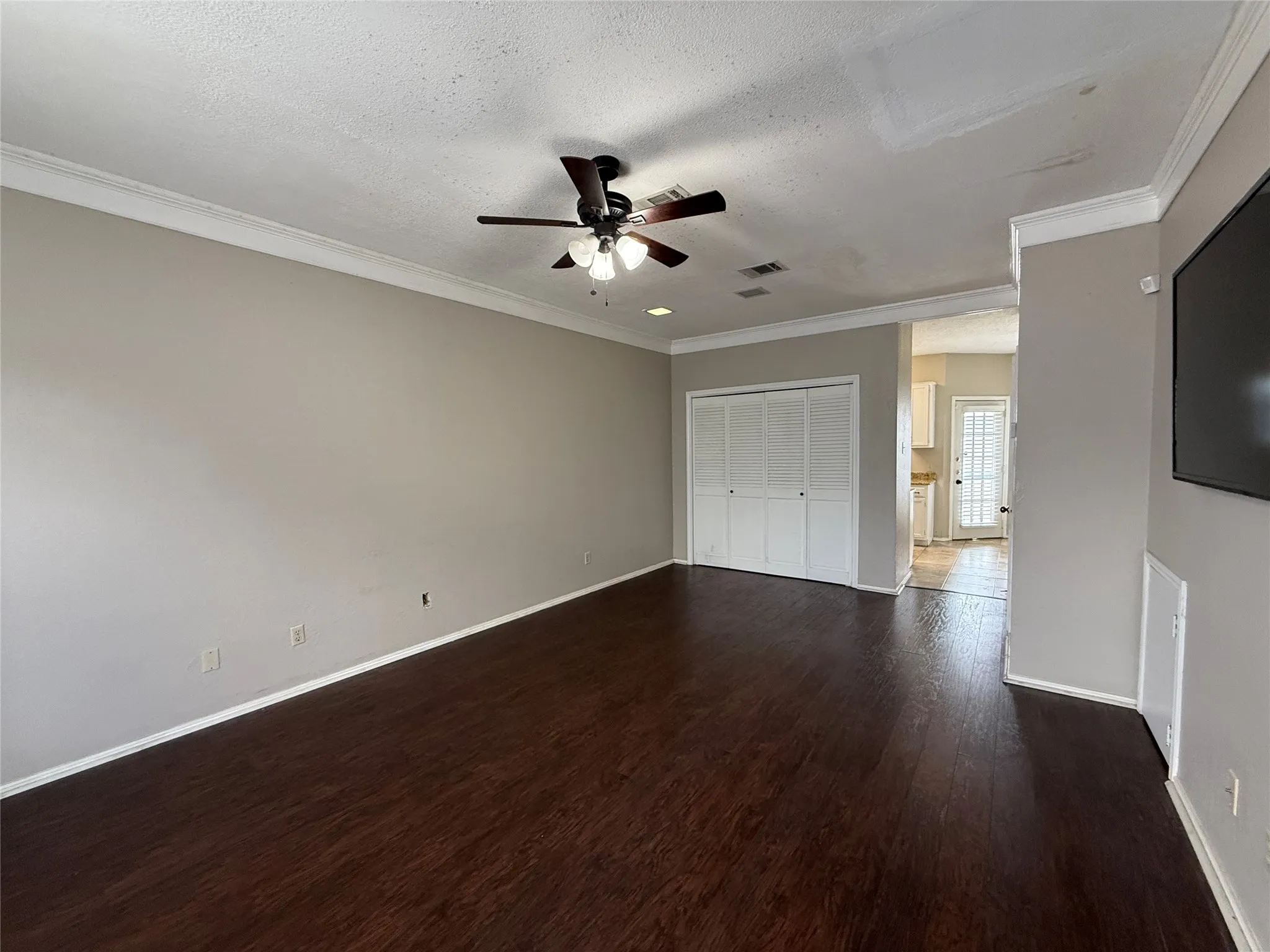 Unfurnished bedroom featuring dark wood-style floors, ornamental molding, a textured ceiling, a closet, and a ceiling fan