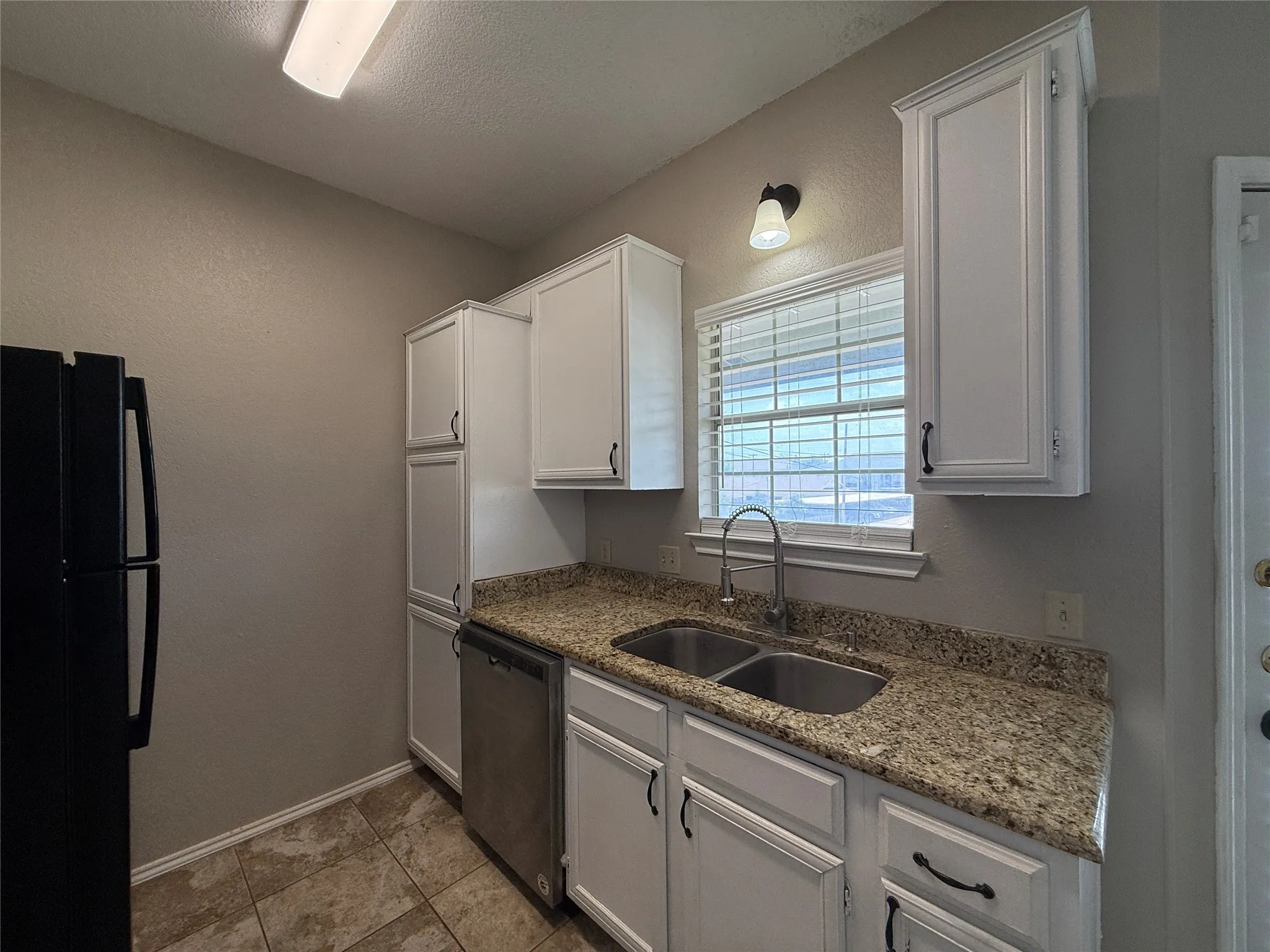 Kitchen featuring freestanding refrigerator, stainless steel dishwasher, white cabinets, light stone counters, and a textured ceiling