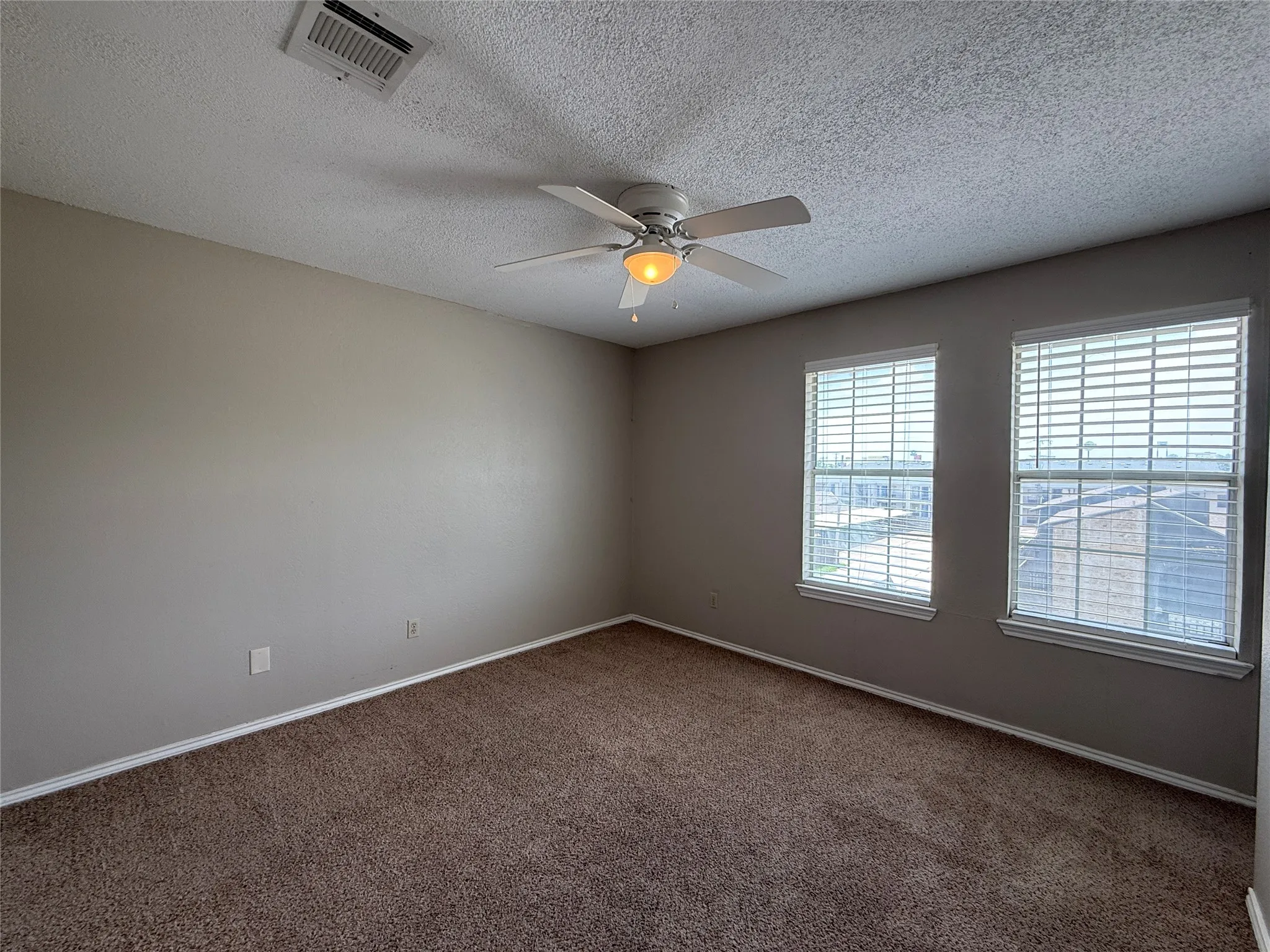 Empty room with plenty of natural light, carpet flooring, a ceiling fan, and a textured ceiling
