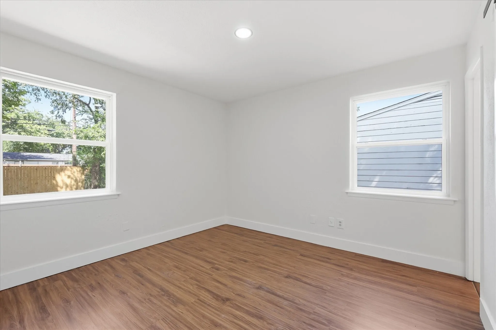 Spacious room featuring wood-finish flooring, recessed lighting, and two windows providing abundant natural light