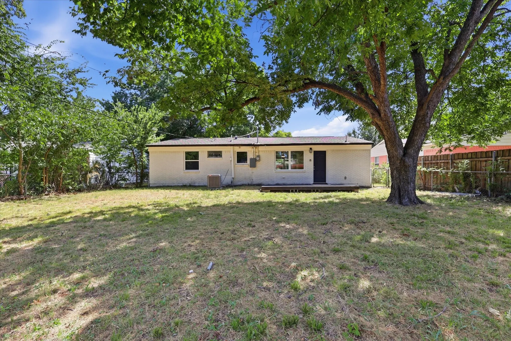 Expansive backyard featuring a mature shade tree, a white painted brick exterior, and a wooden deck