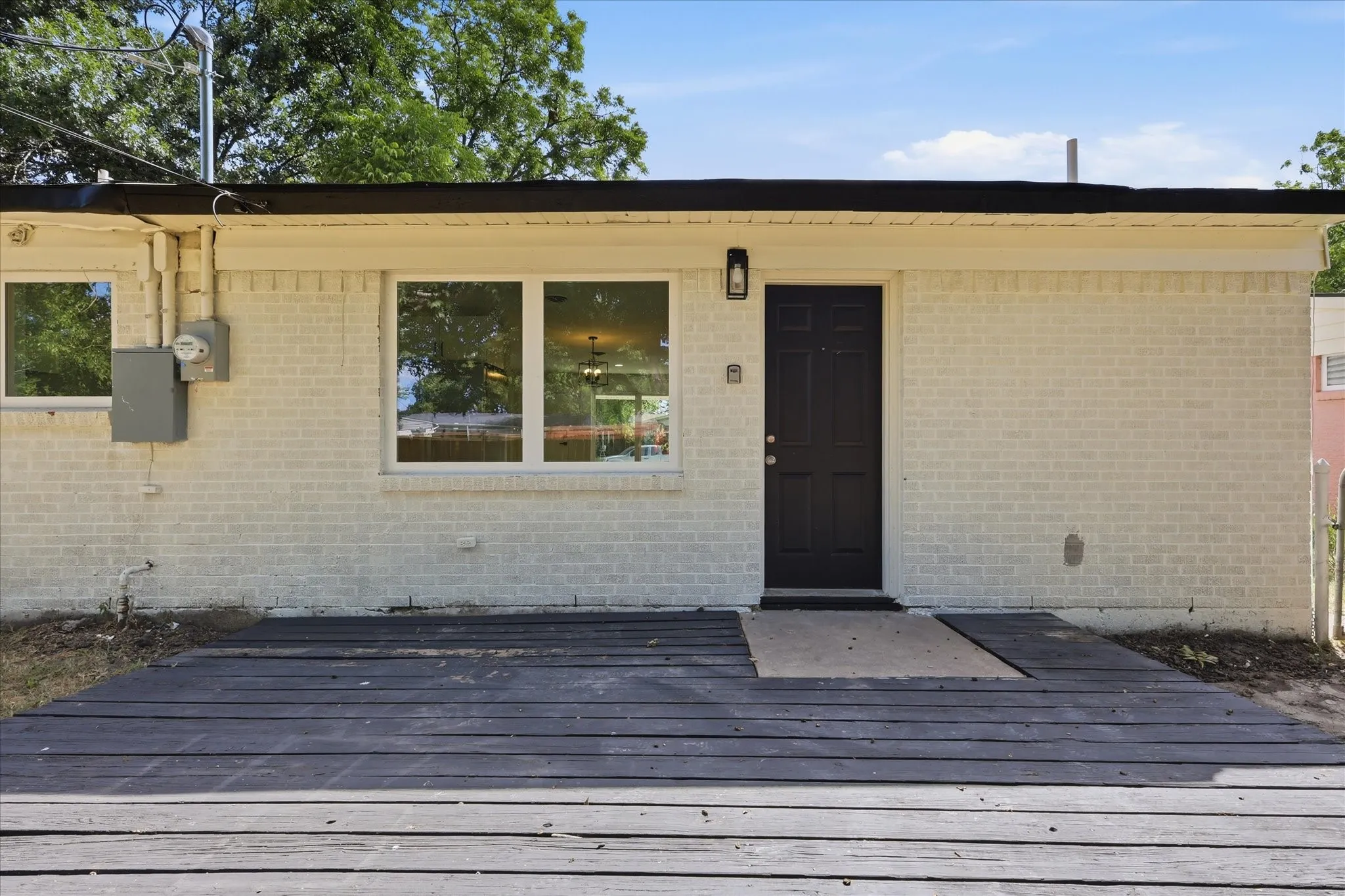 Exterior featuring painted brick siding, a dark paneled entry door with an overhead sconce, and white-framed windows