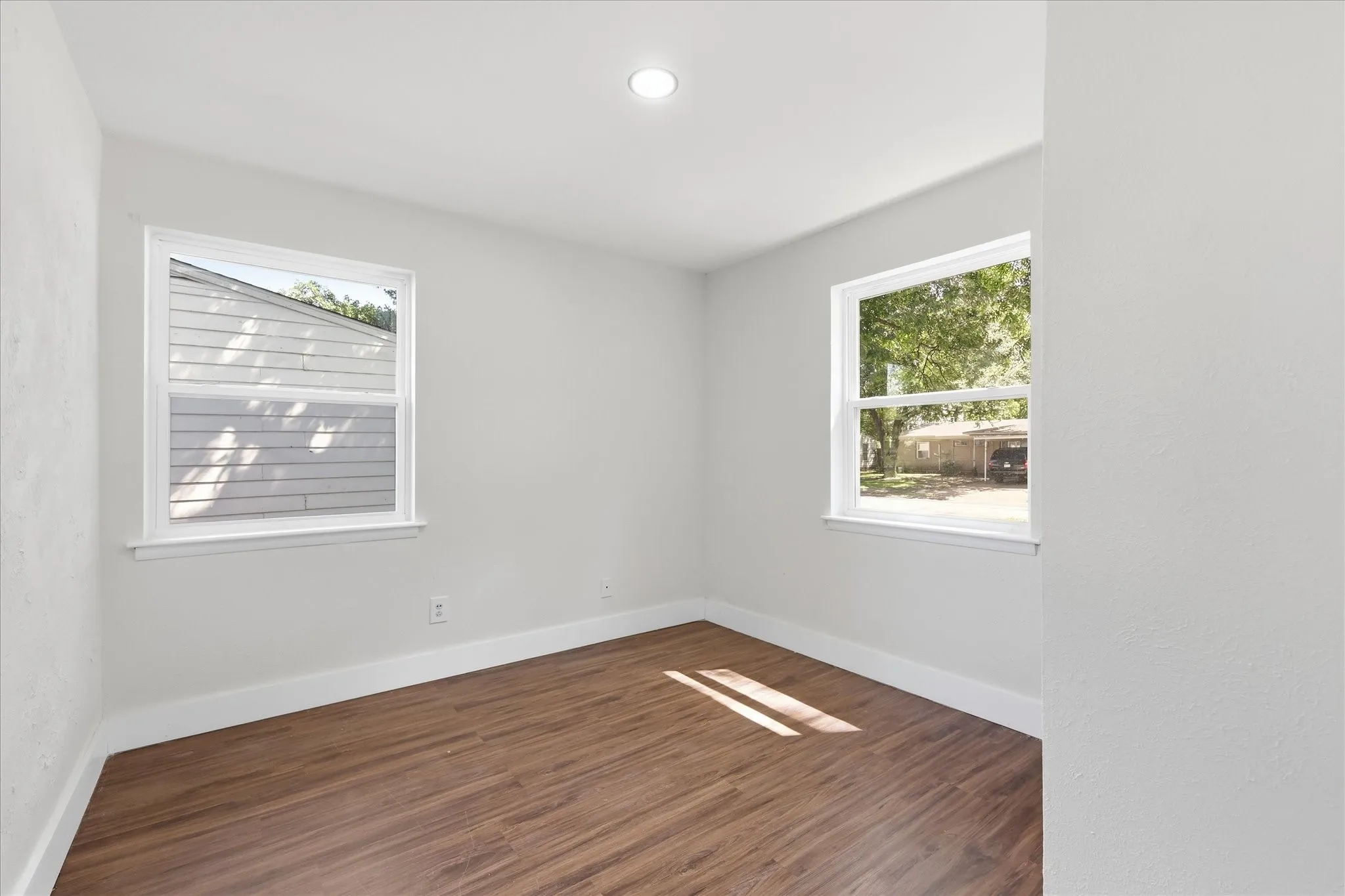 Bright room featuring wood-finish flooring, crisp white baseboards, and two windows with white frames