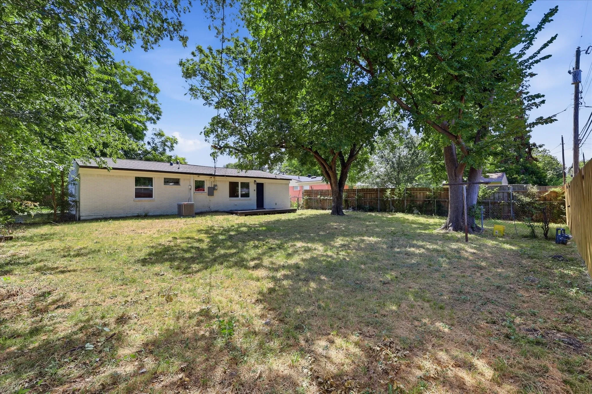 Expansive backyard featuring mature trees, a wooden privacy fence, chain-link fencing, and a white-painted exterior with multiple windows