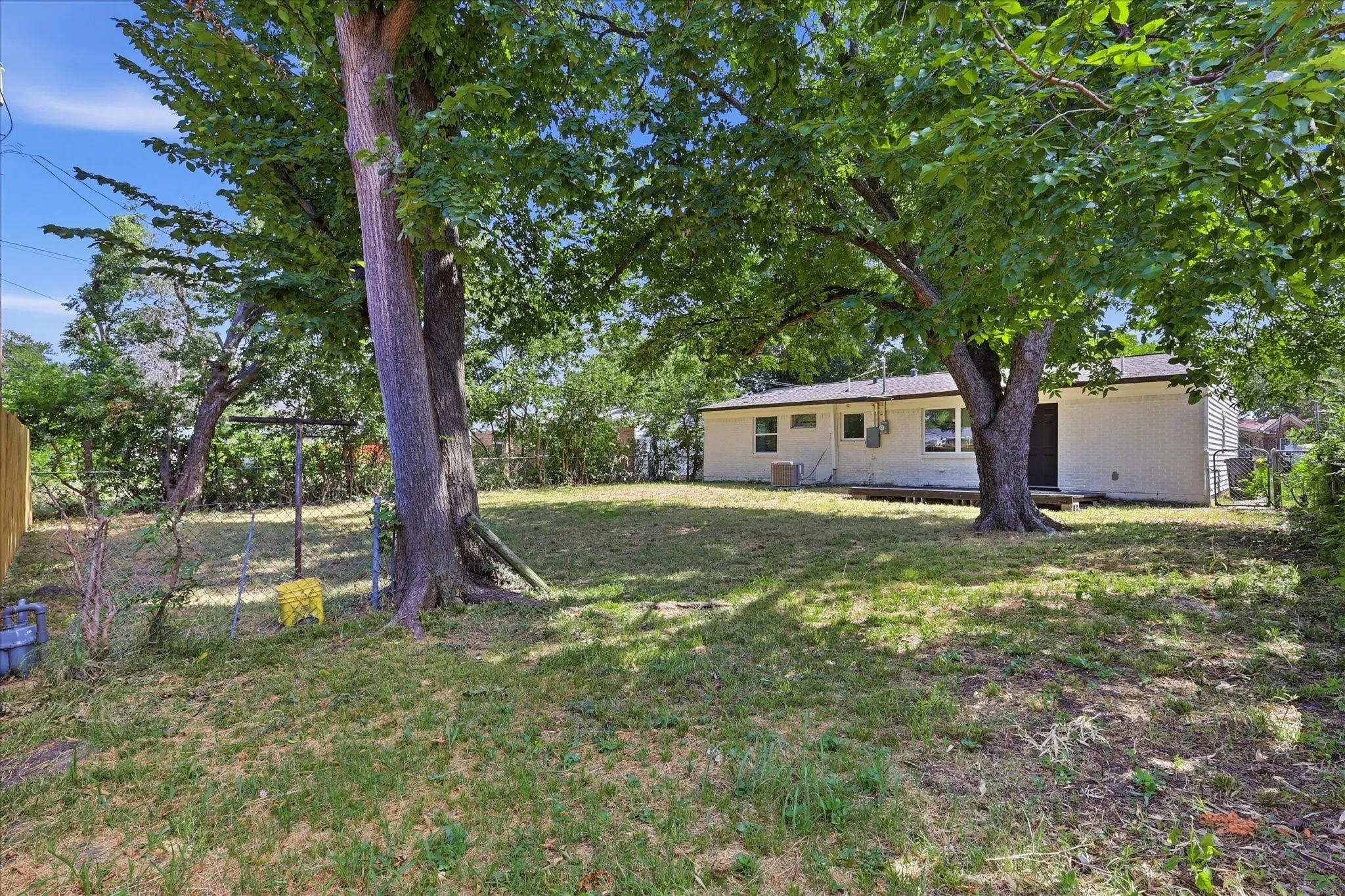 Spacious backyard featuring established trees, a grassy area, and a light-colored siding exterior
