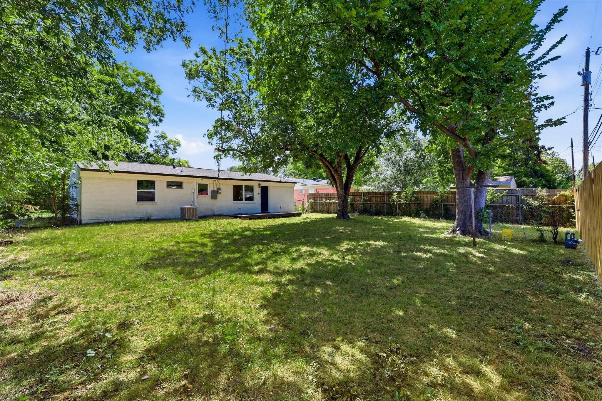 Expansive backyard featuring a large green lawn, mature trees, and a perimeter fence