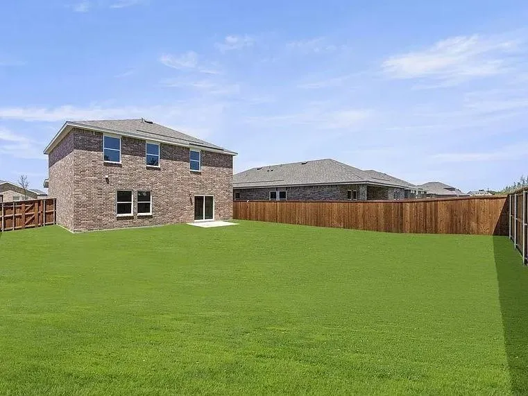 Expansive rear lawn featuring a two-story brick exterior, private wood fencing, multiple windows, and a ground-level patio with sliding glass door access