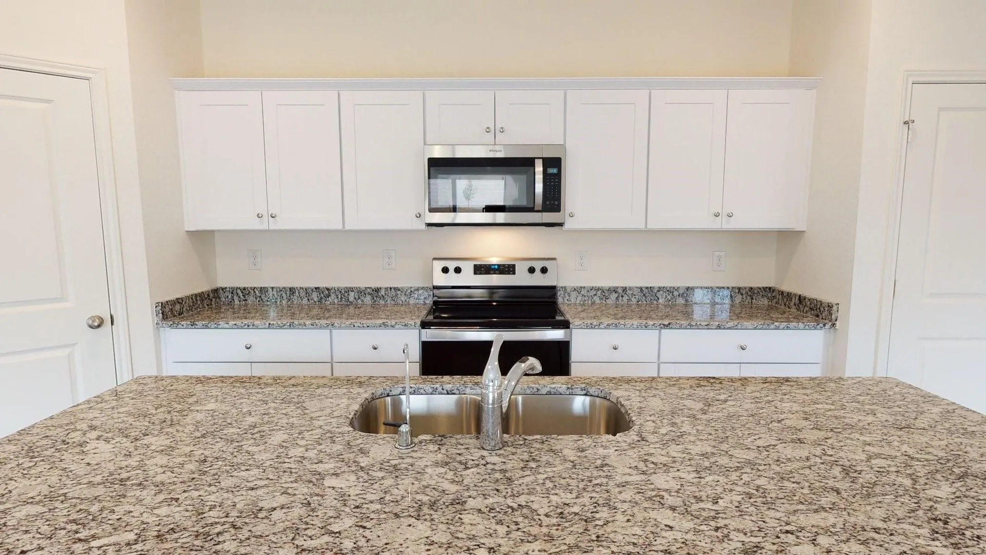 Kitchen featuring an island with an undermount sink, granite countertops, white cabinetry, a stainless steel range, and an over-the-range microwave