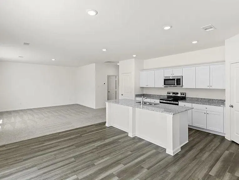 Open-concept kitchen and living area featuring wood-finish flooring, white cabinetry, stainless steel appliances, granite countertops, and recessed lighting
