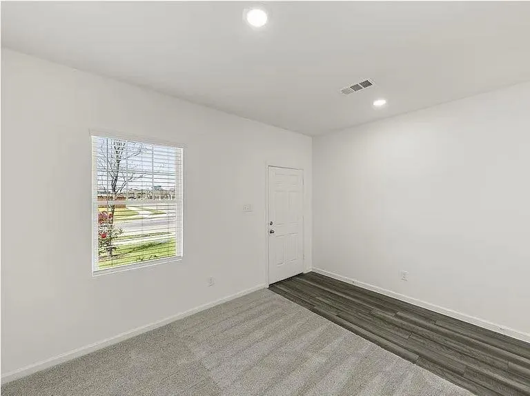 Open room featuring a window with blinds, a white paneled door, recessed lighting, and a blend of gray carpet and wood-finish flooring