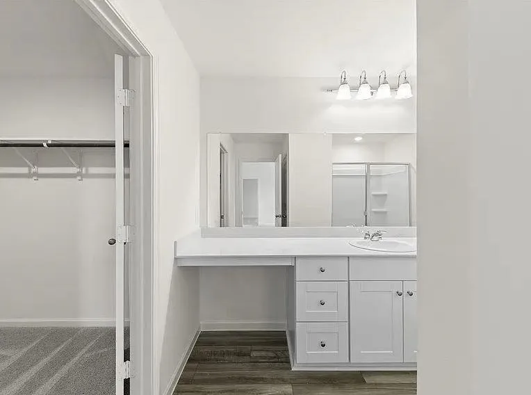 White vanity with integrated sink, four-light fixture, and wood-finish flooring