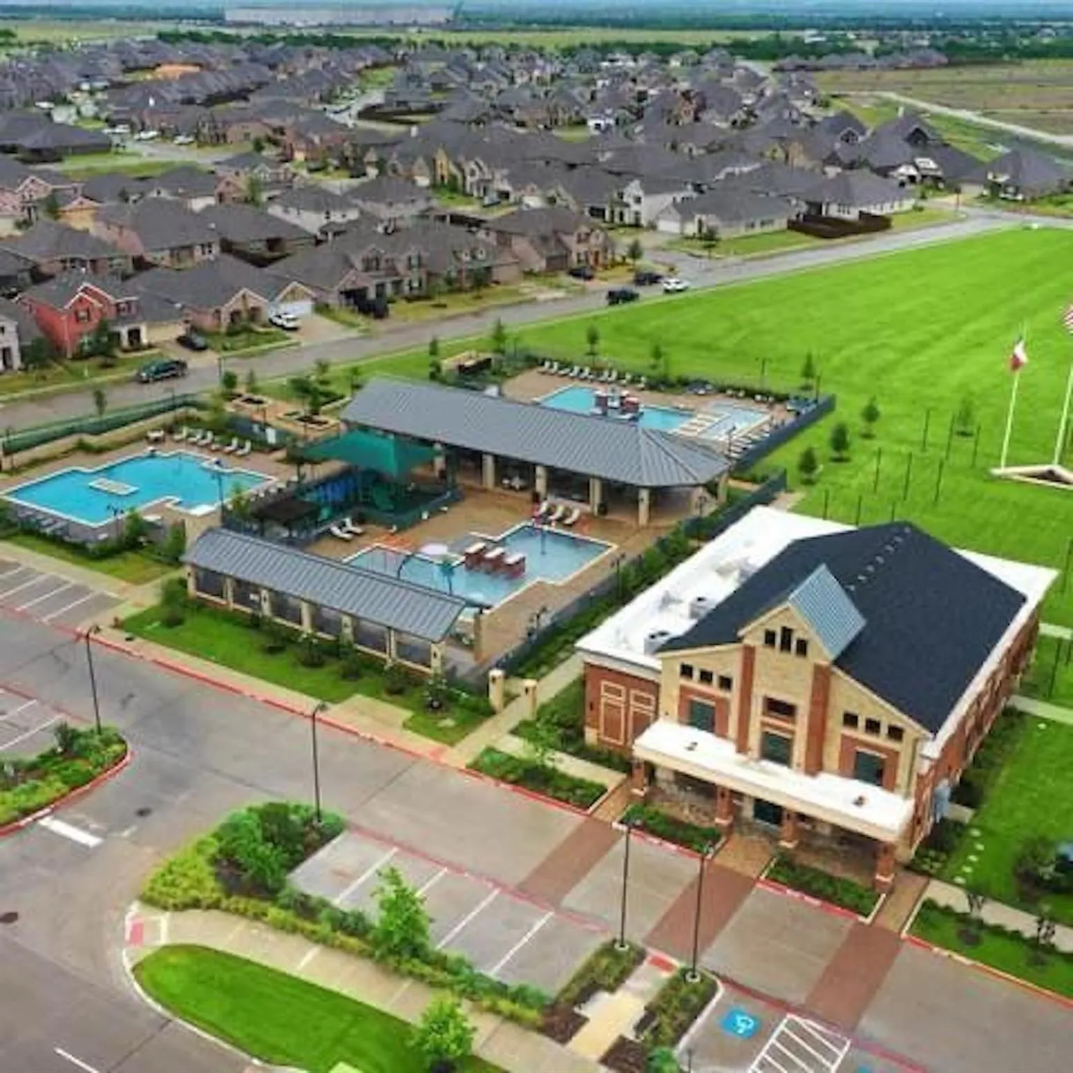 Community amenity center featuring multiple pools, expansive green space, and a dedicated parking area